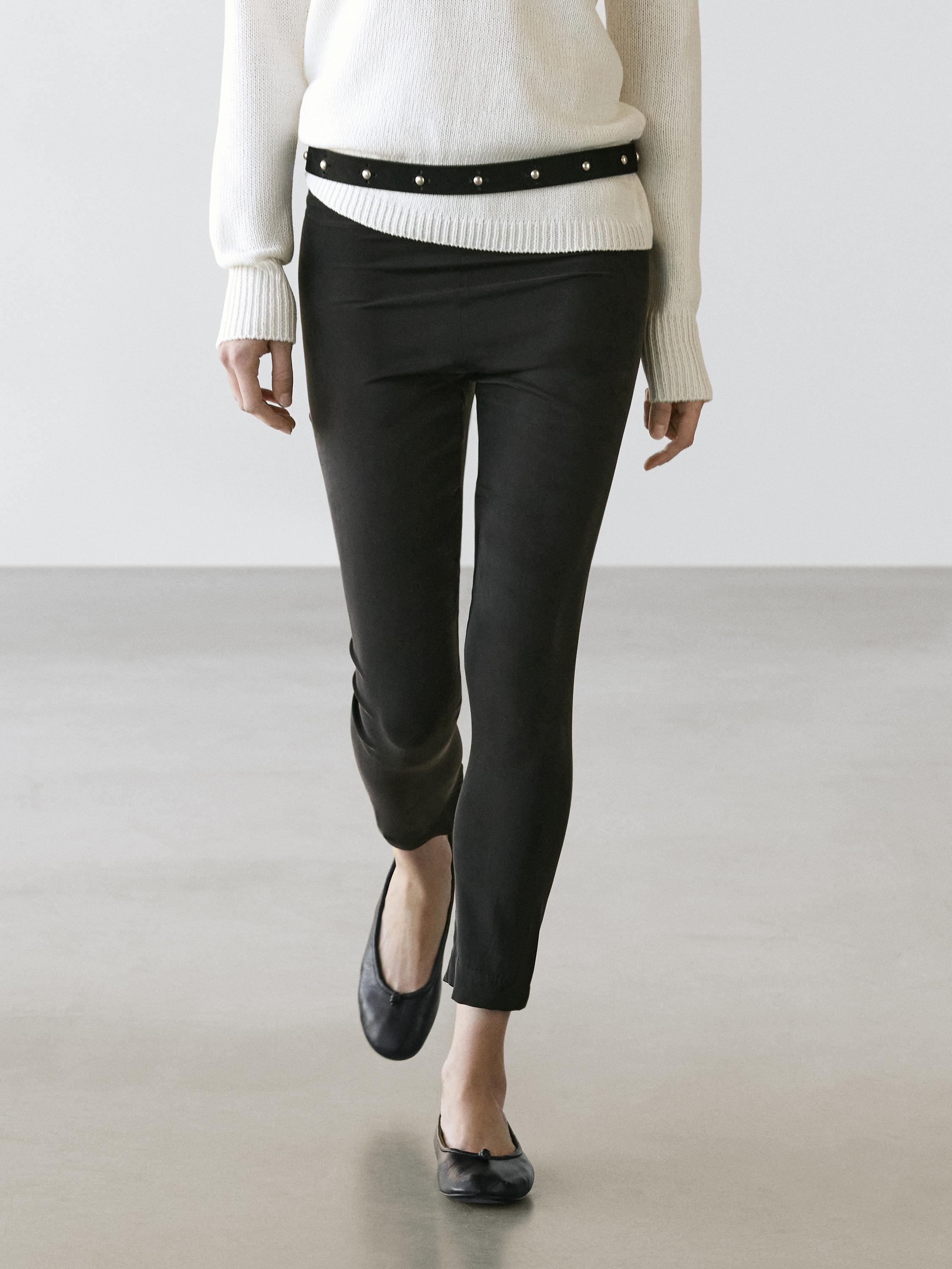 Conjunto de calças legging pretas e camisola branca com cinto preto de tachas.