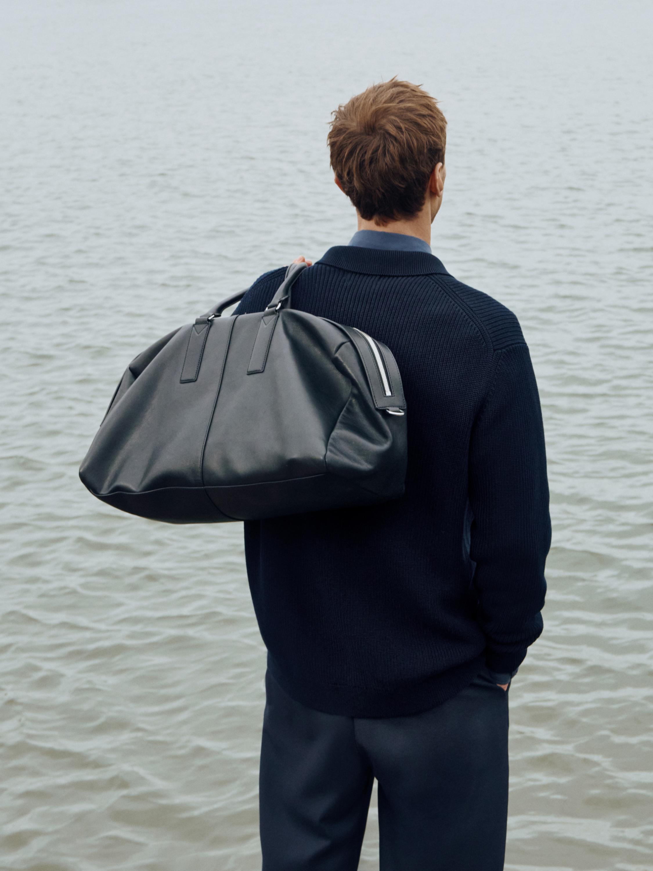 Schwarzes Reisetaschen-Set mit Griffen und Reißverschluss, über der Schulter getragen.