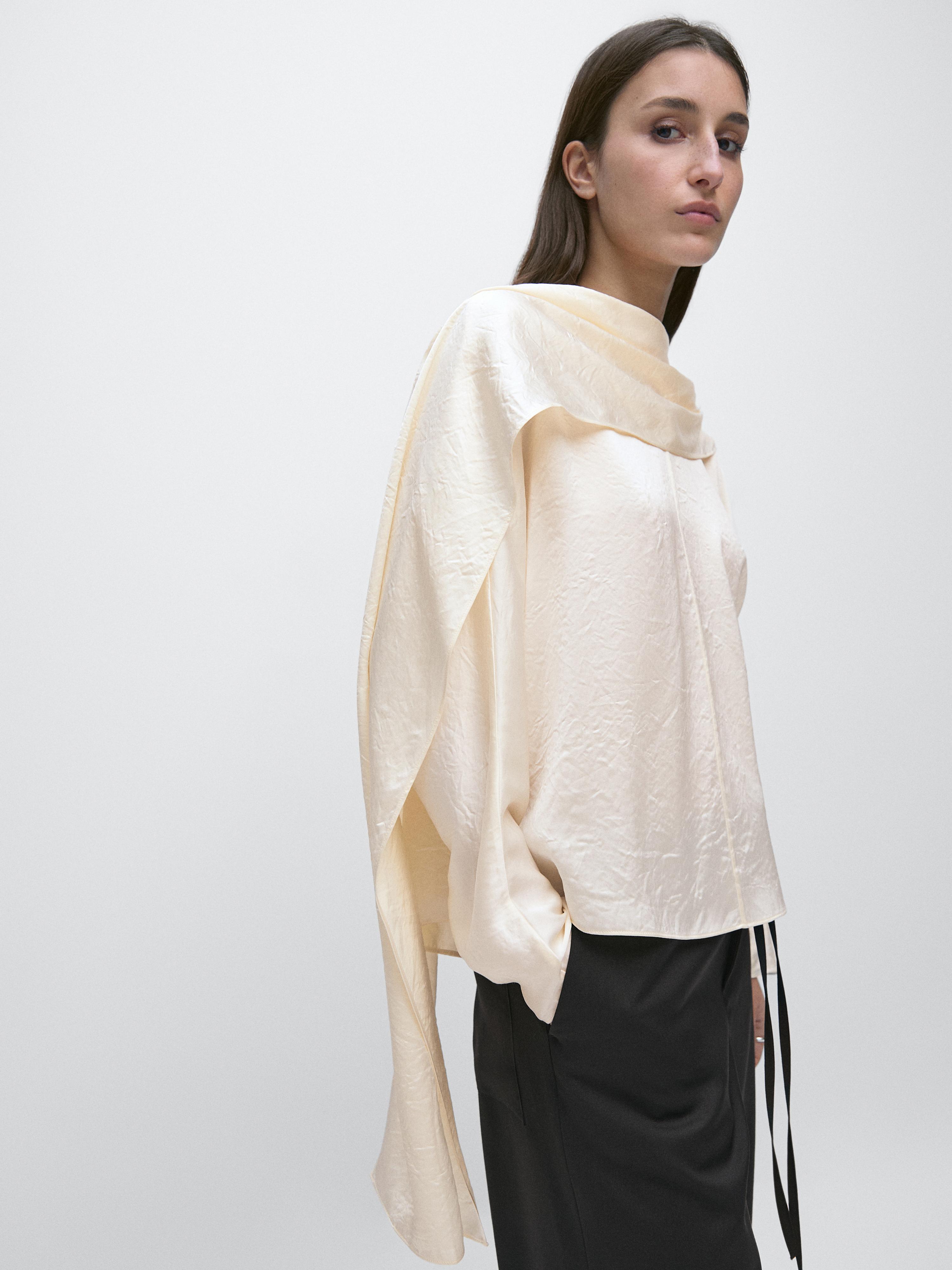 "Medium shot of a flowy blouse with an overlay, an asymmetrical design, and a loose fit, paired with black pants."