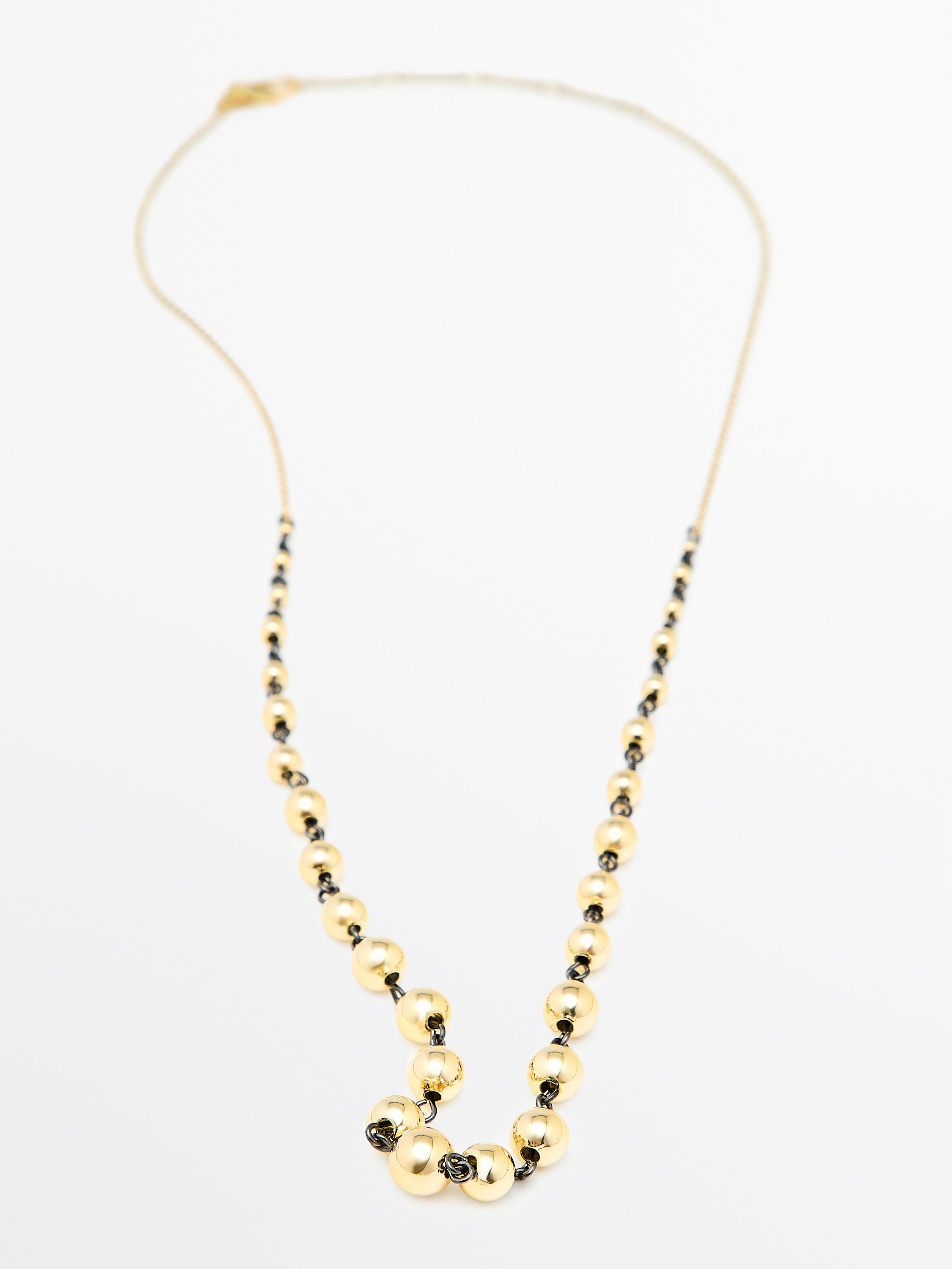 Colar dourado con abelorios esféricos e detalles escuros nos elos.