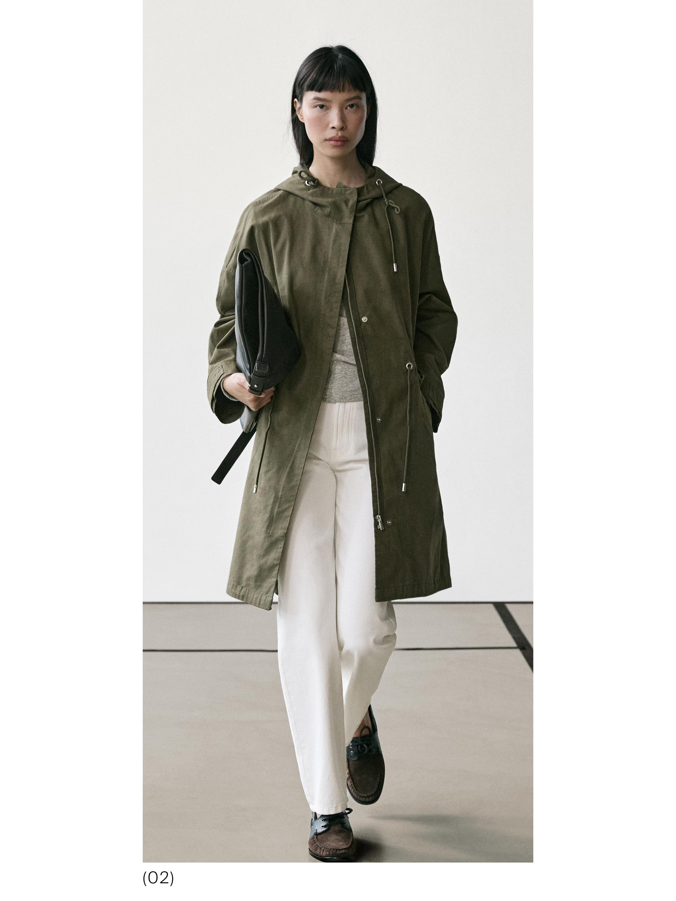 Komplet pallto jeshile me kapuç, pantallona të bardha dhe këpucë kafe. Xhep anësor i dukshëm në pallto.