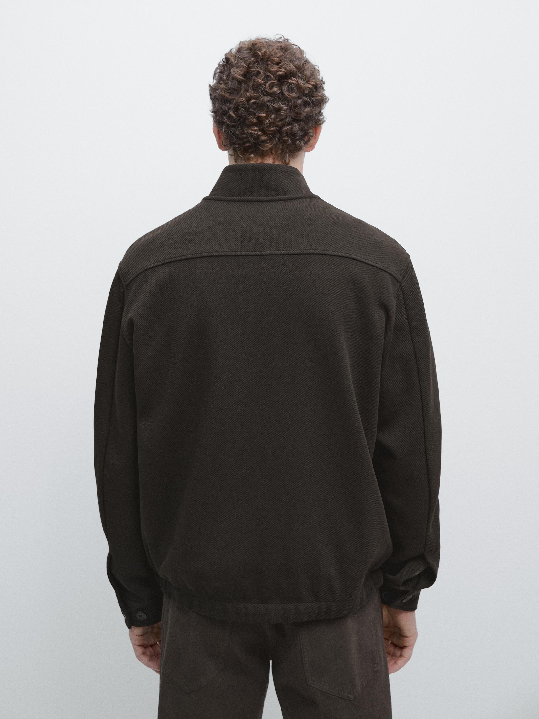 Vista posterior de chaqueta marrón con cremalleira e colo alto. Mangas longas con puños abotoados.