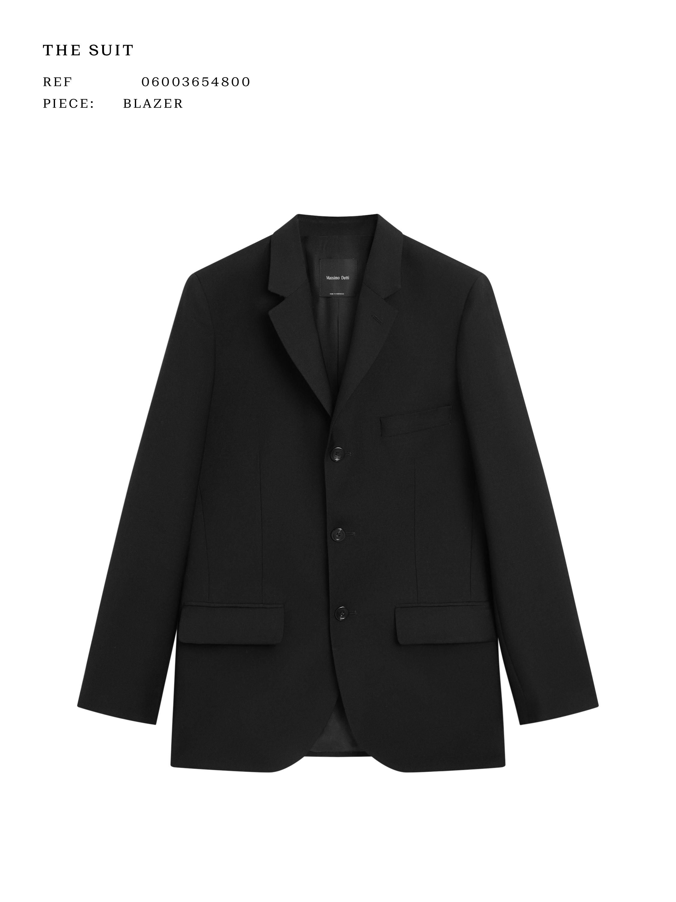 Front view of a black blazer with three buttons, classic lapels, and front flap pockets. Visible text: "THE SUIT".