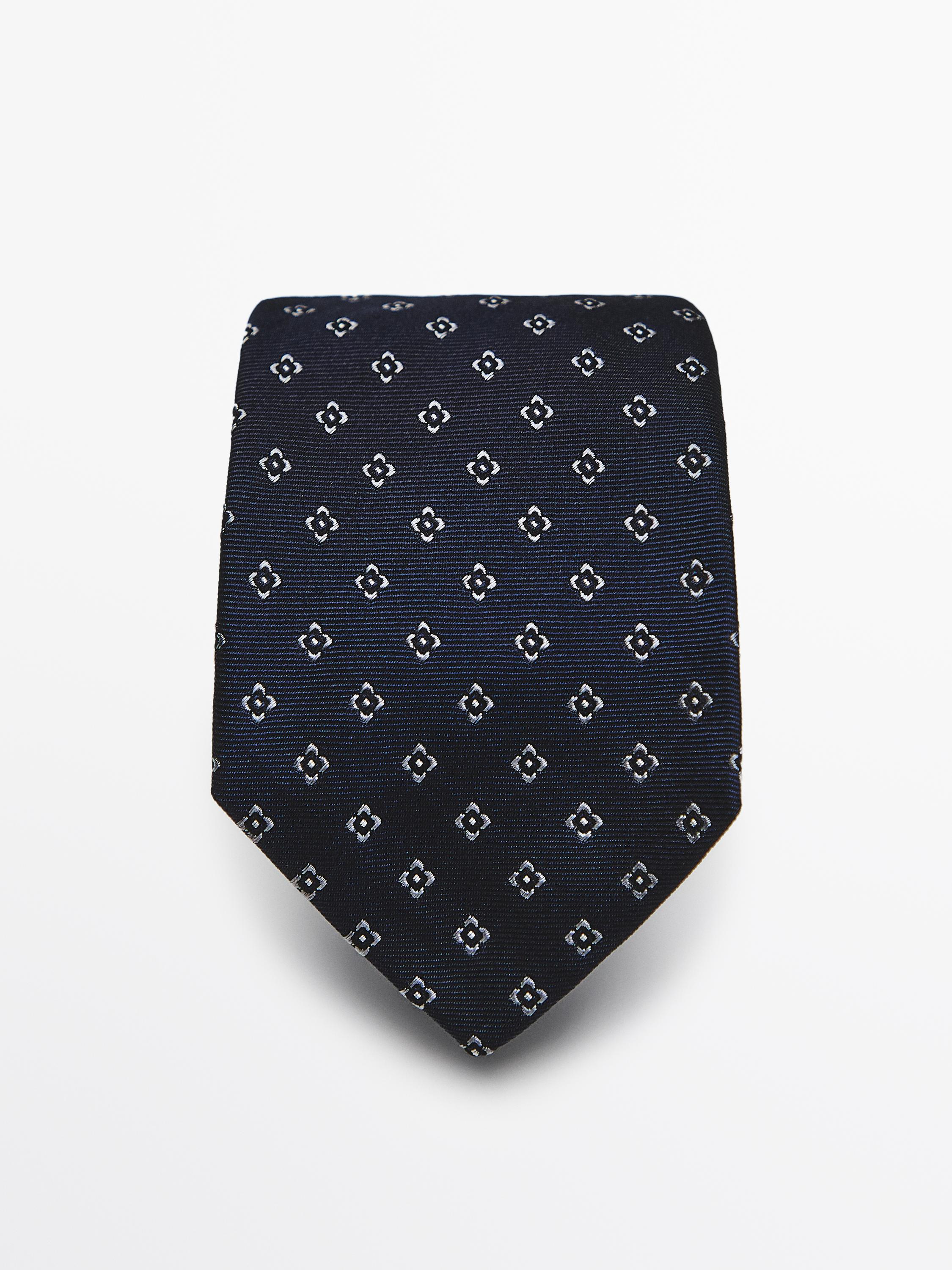 Вид спереди темно-синего галстука с принтом из мелких белых геометрических узоров.
