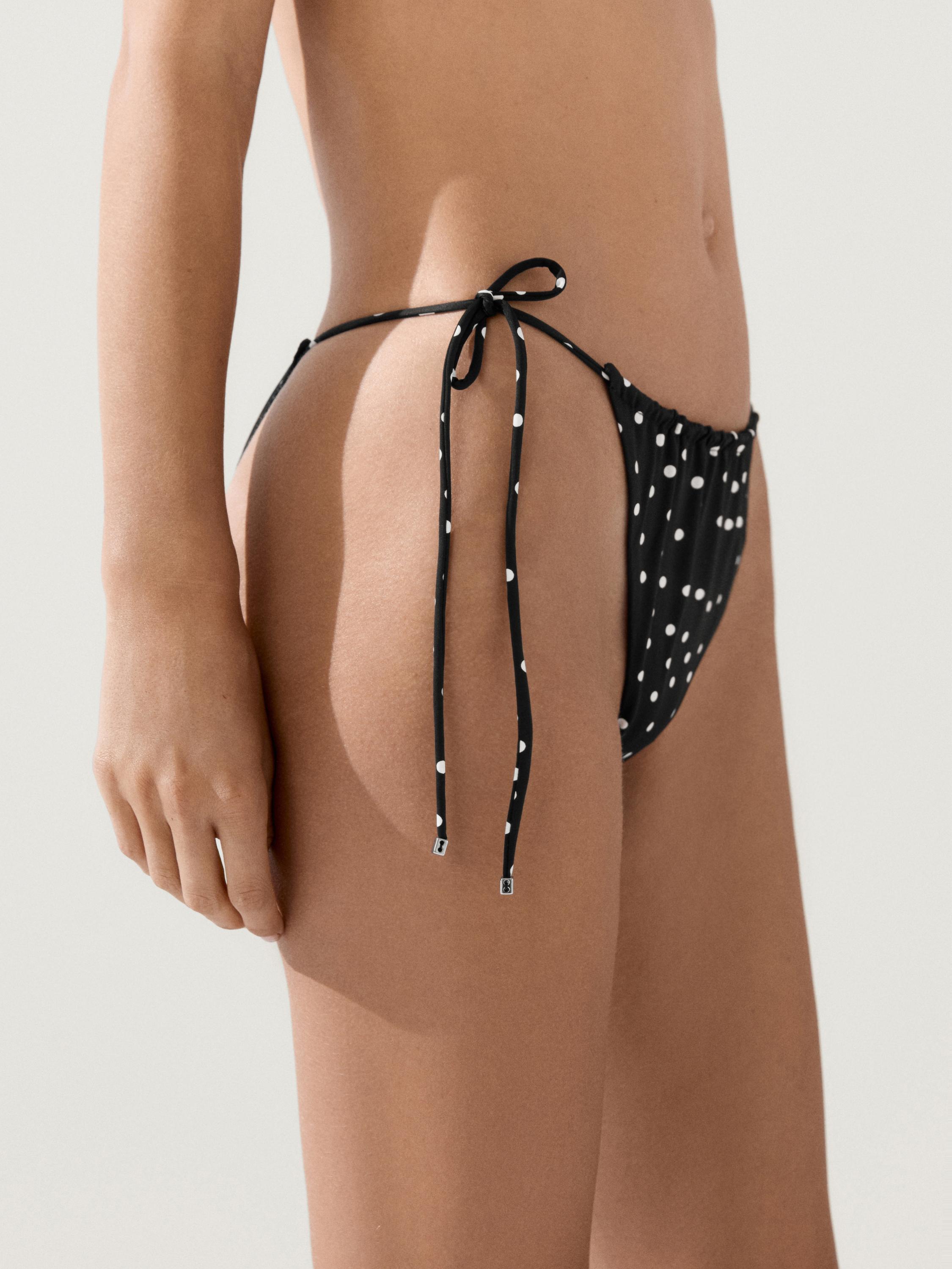 Plano medio de braguita de bikini negra con lunares blancos y lazos laterales.