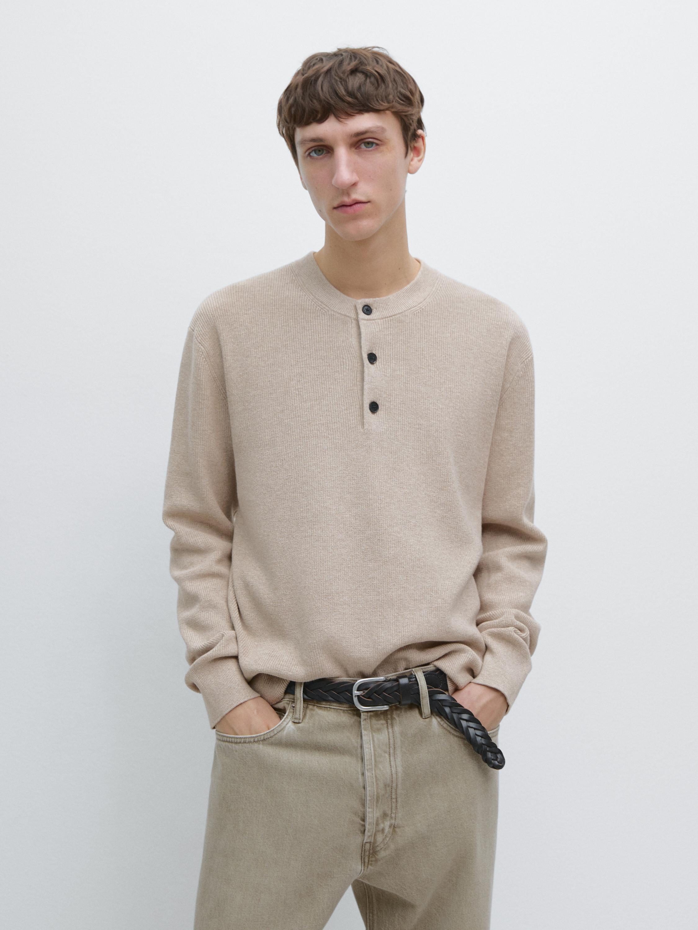 Beige crew-neck sweater set with black buttons, beige pants, and black braided belt.