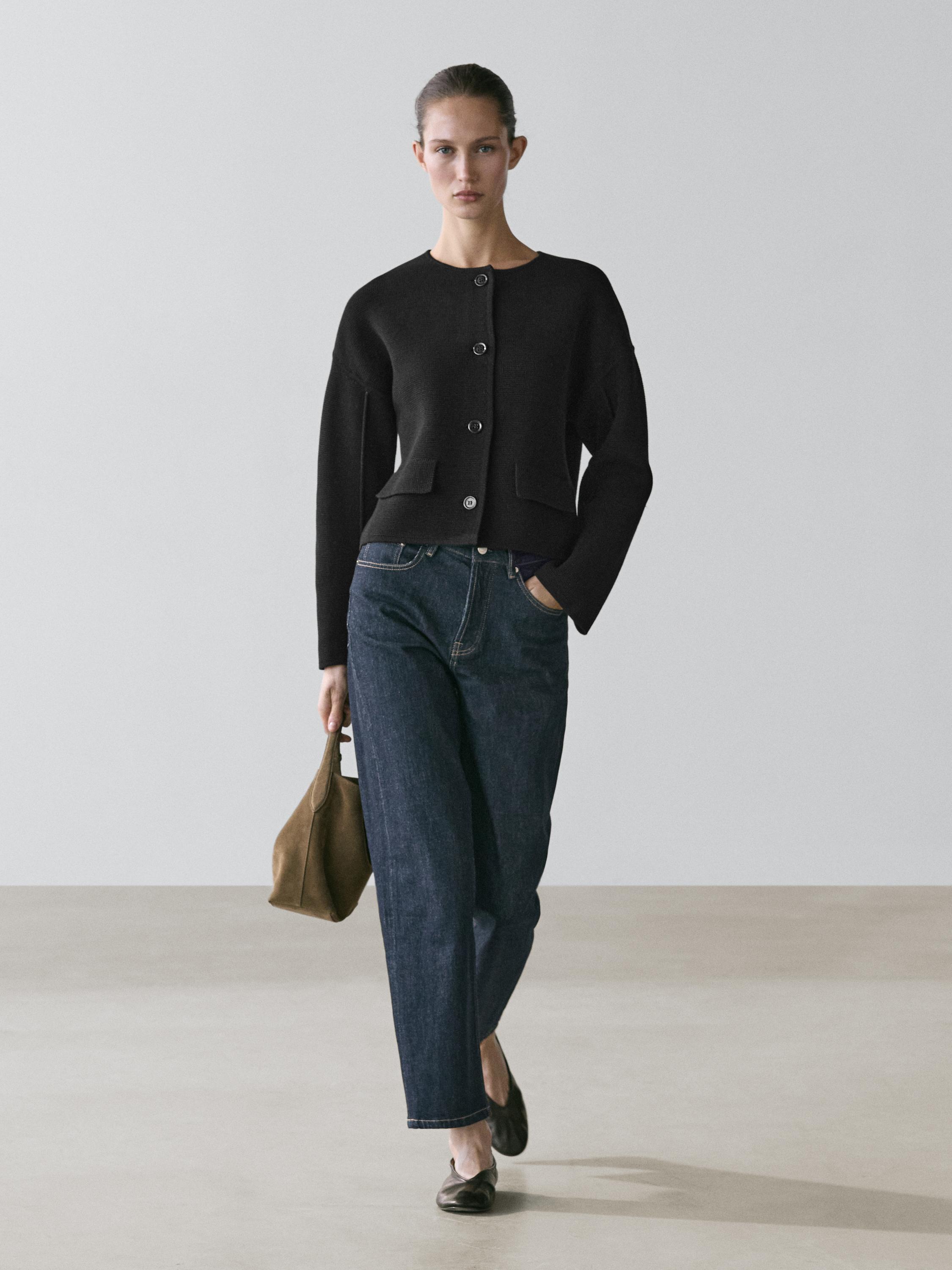 طقم كارديغان أسود بأزرار كبيرة وجيوب أمامية، بنطال جينز أزرق، وحذاء فلات أسود.