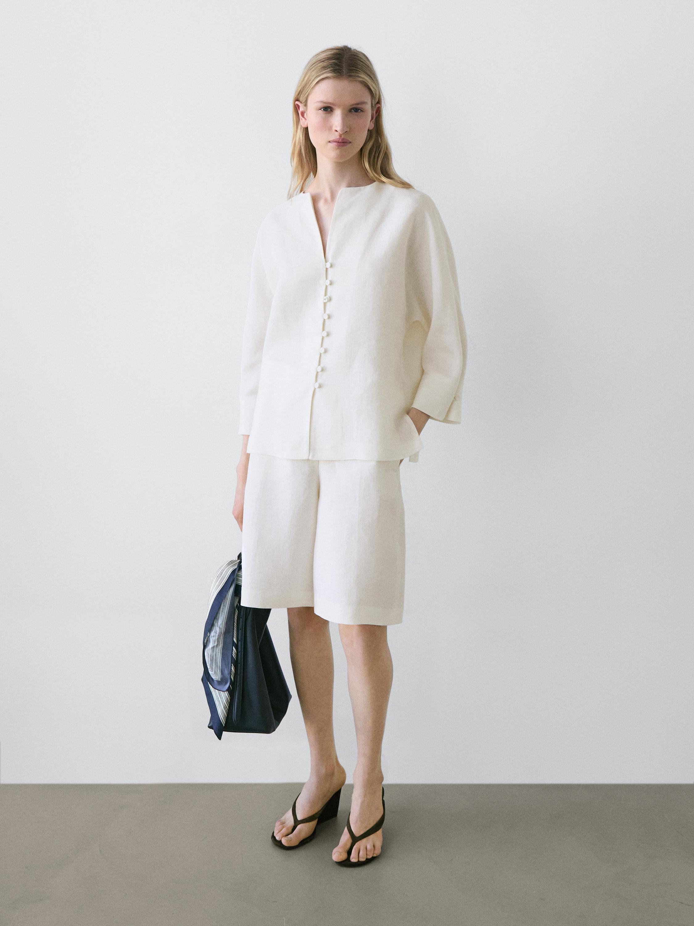 Conjunto de blusa blanca con botones frontales y mangas 3/4, shorts blancos hasta la rodilla y sandalias negras.