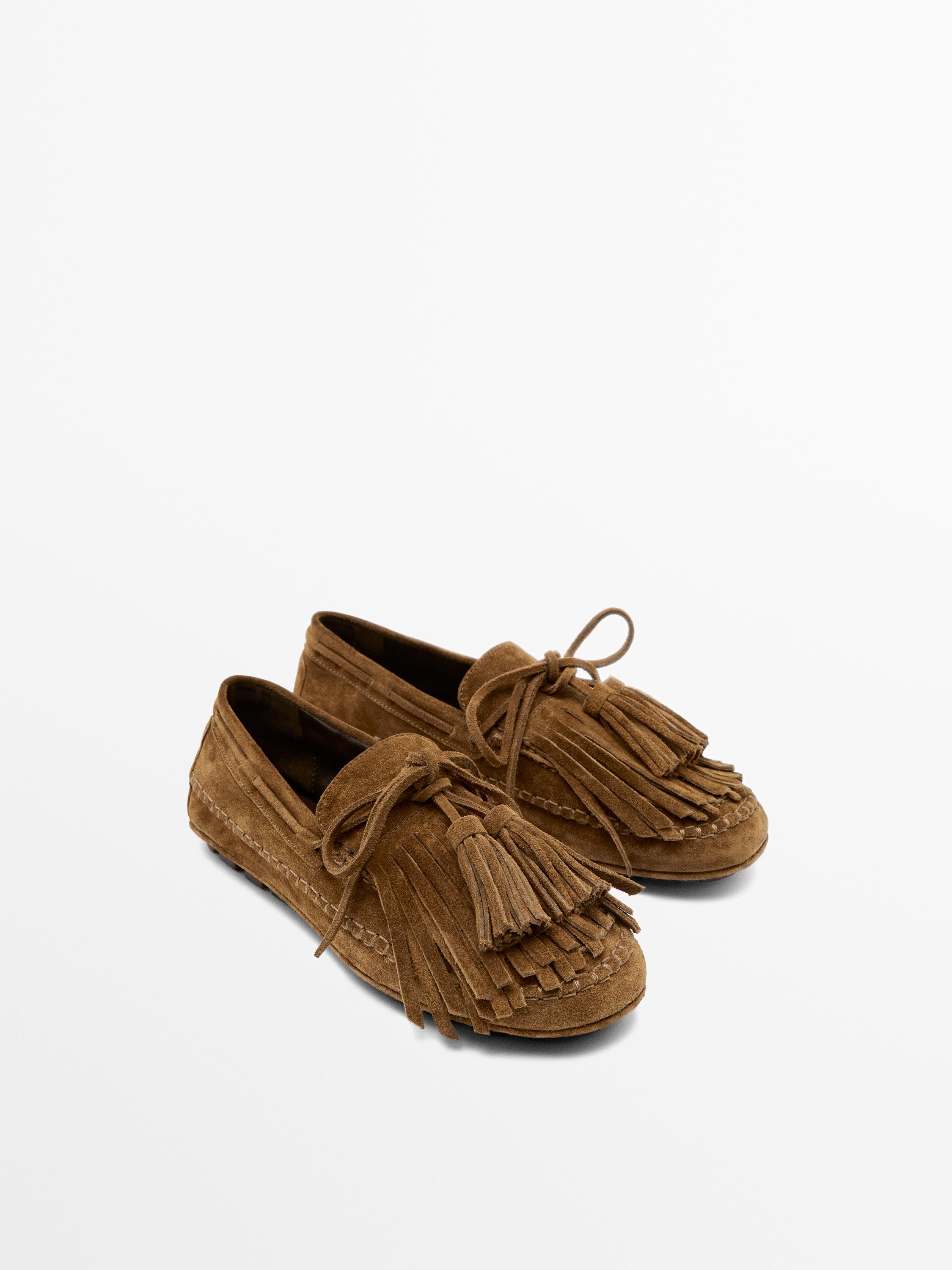Front view of leather-colored loafers with fringe and tassels on the upper, visible stitching and flat sole.