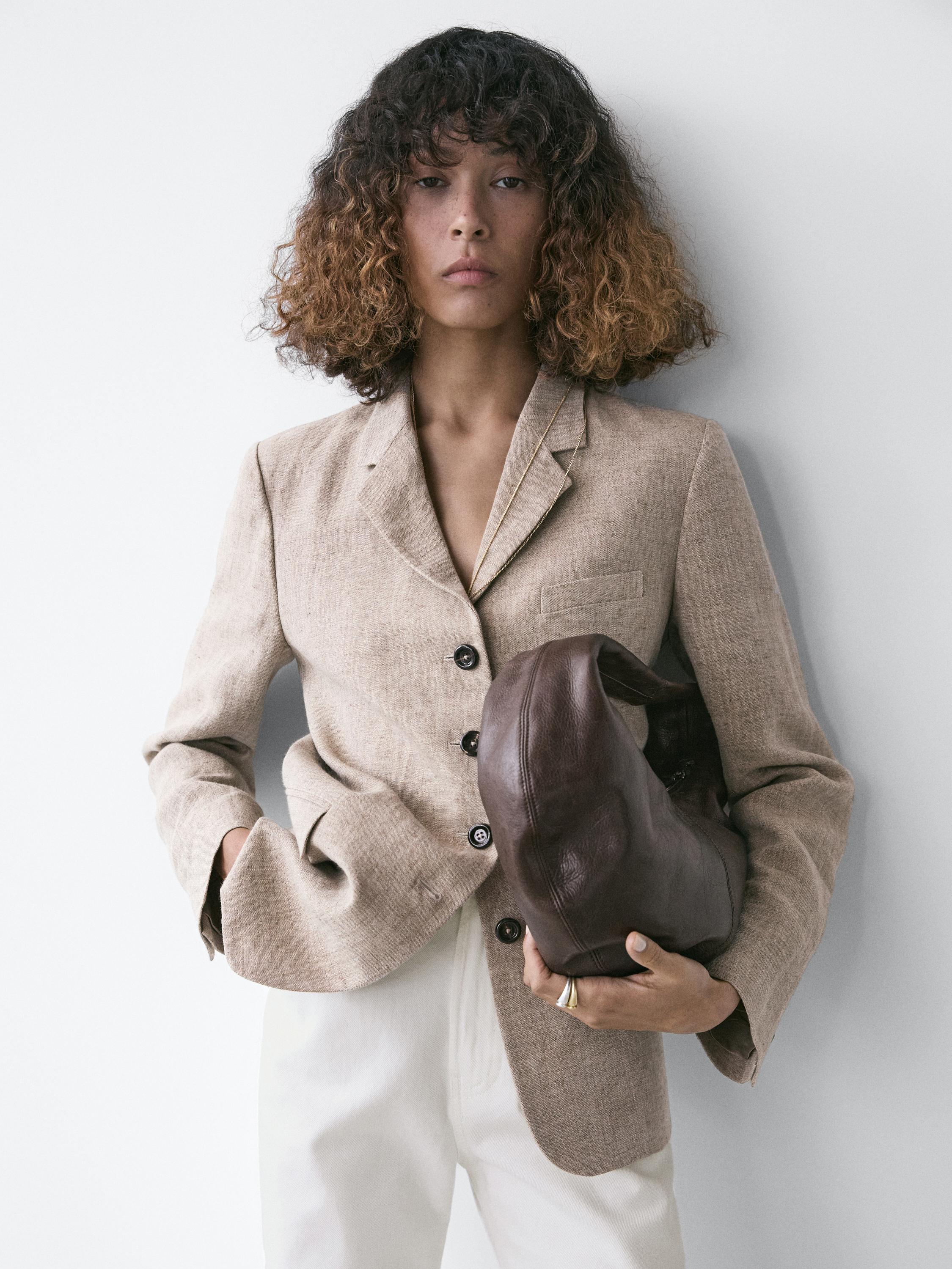 Conjunto de blazer bege com bolsos laterais e botões frontais, combinado com calça branca.