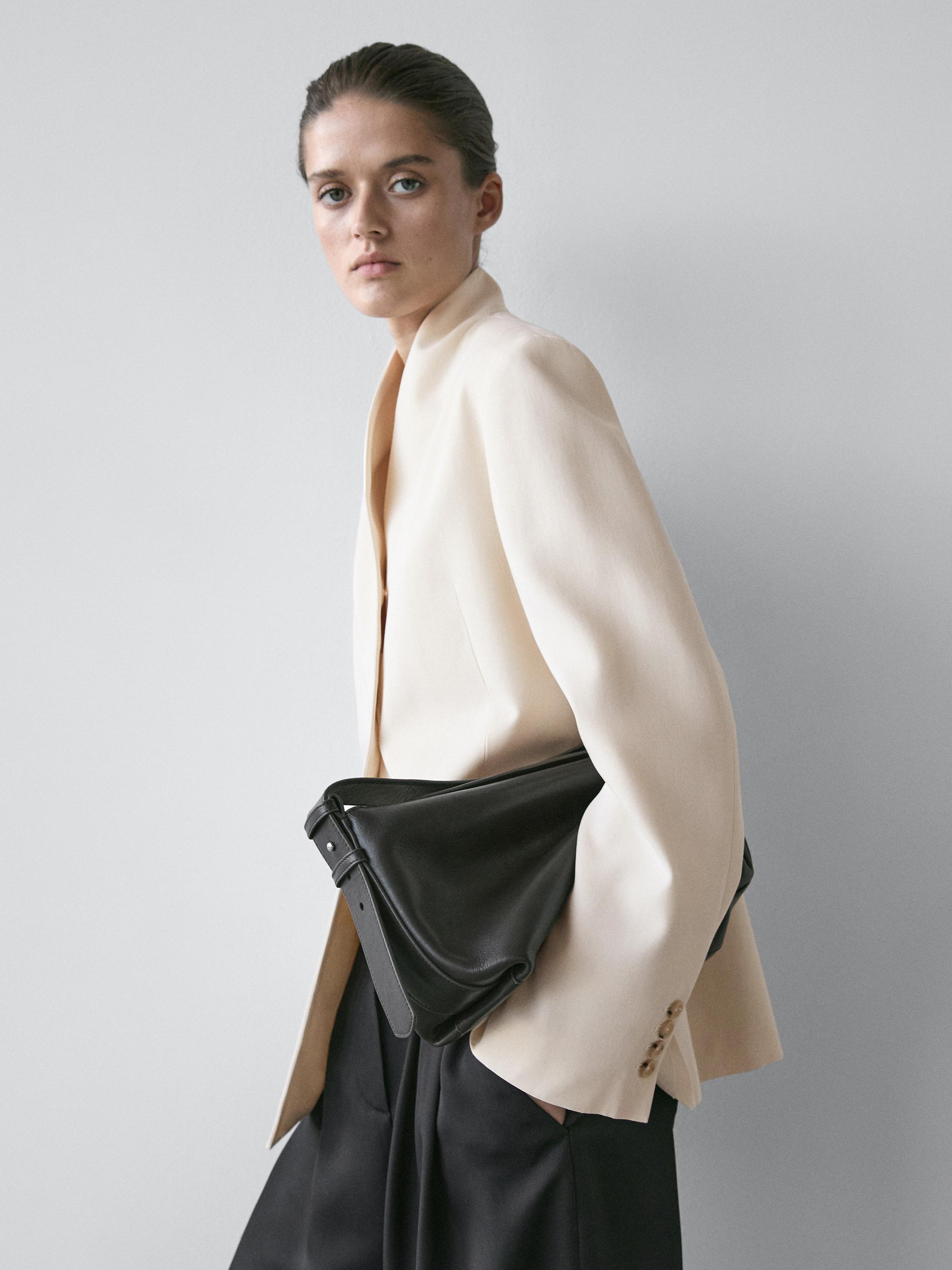 Raw high-neck blazer set with buttoned sleeves and black pants.