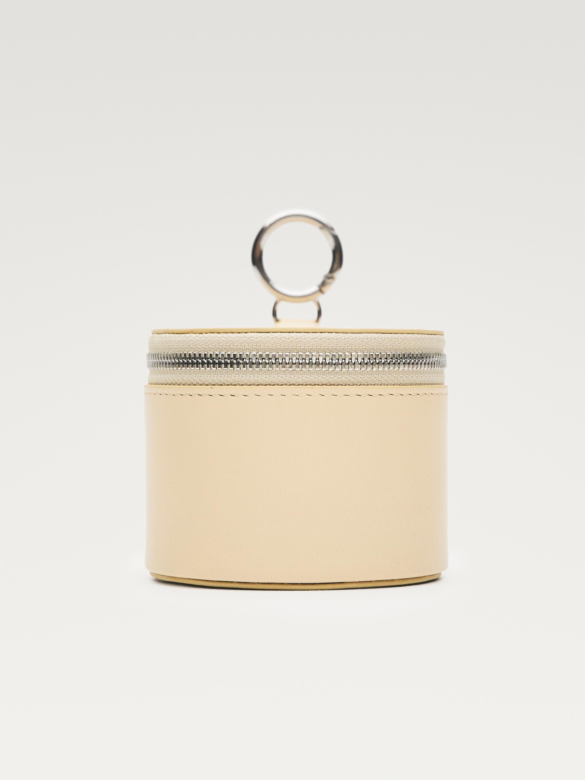 지퍼 잠금장치와 상단에 금속 고리가 있는 바닐라색 지갑의 전면 모습.