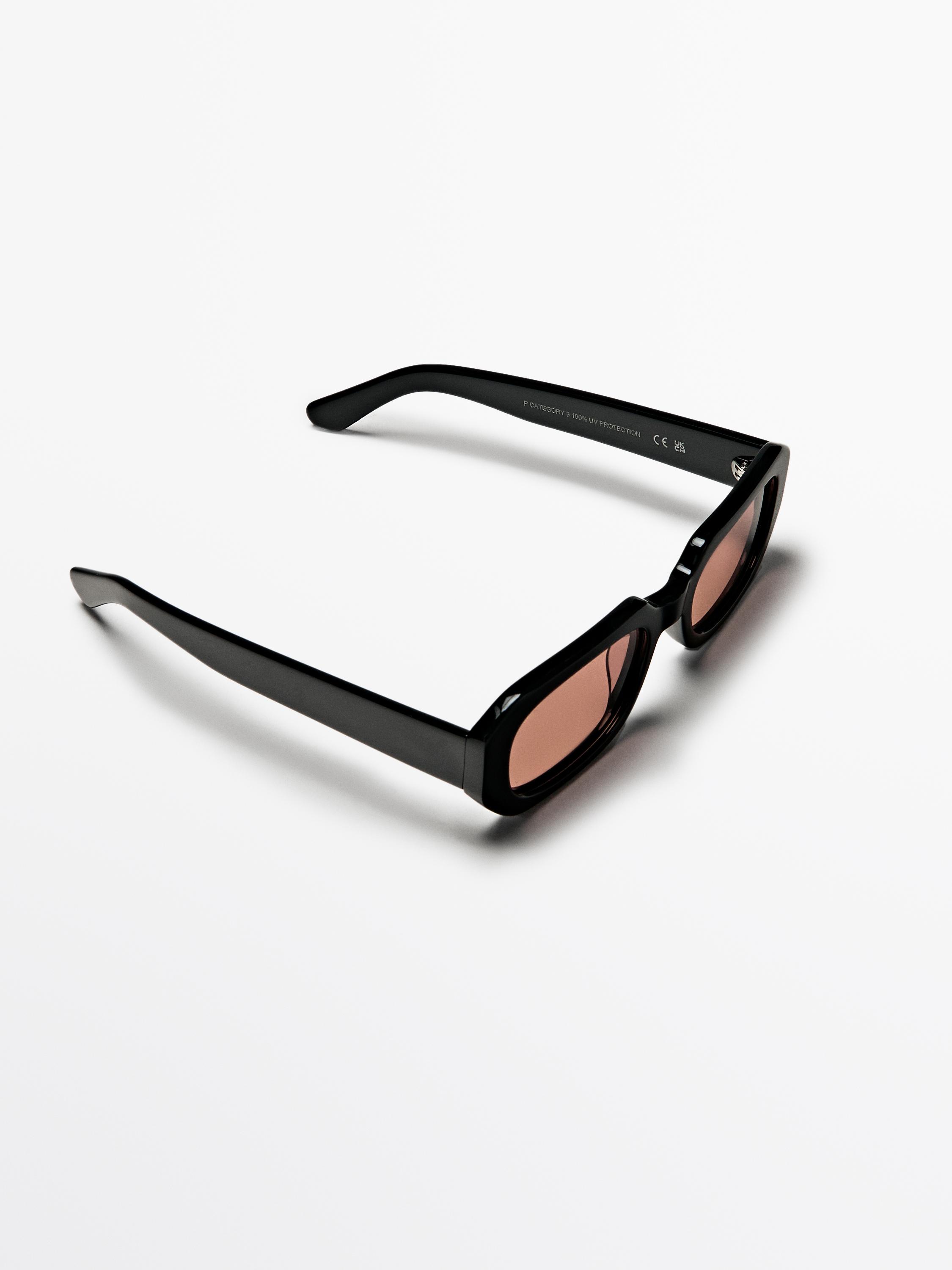 Eguzkitako betaurreko beltzak, armadura angeluzuzenarekin eta kristal tindatuekin. Testua patillan: "100% UV PROTECTION".