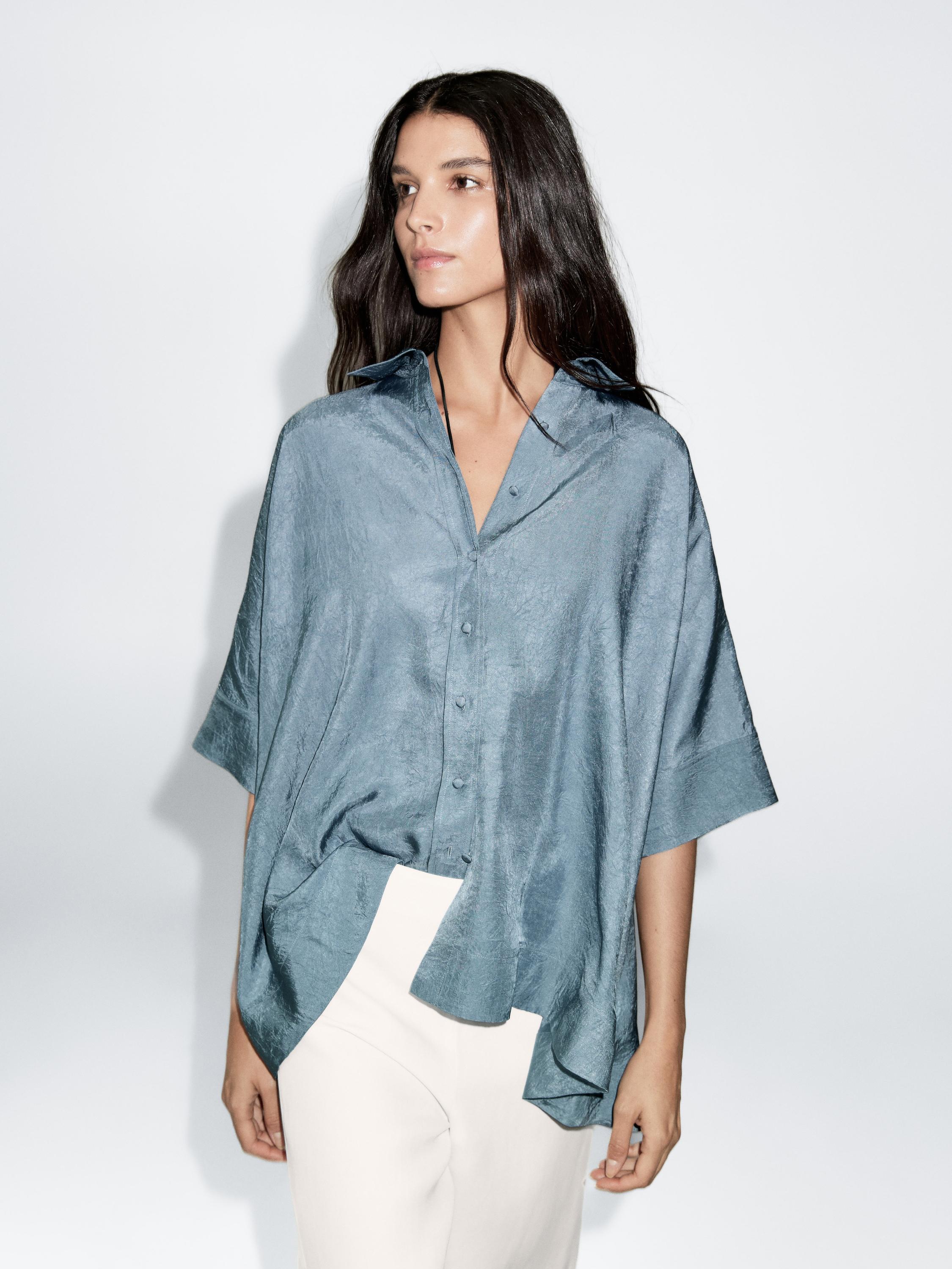 طقم بلوزة فضفاضة زرقاء فاتحة بأزرار مغطاة بالقماش وبنطال أبيض.