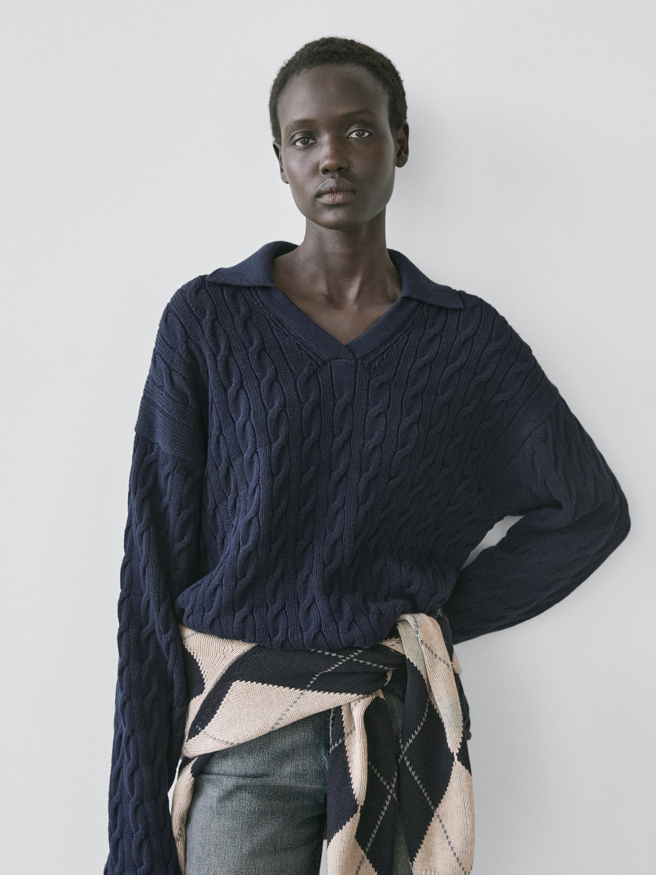 Середній план темно-синього джемпера з коміром поло та плетінням, на талії зав'язаний бежево-синій светр з ромбами.