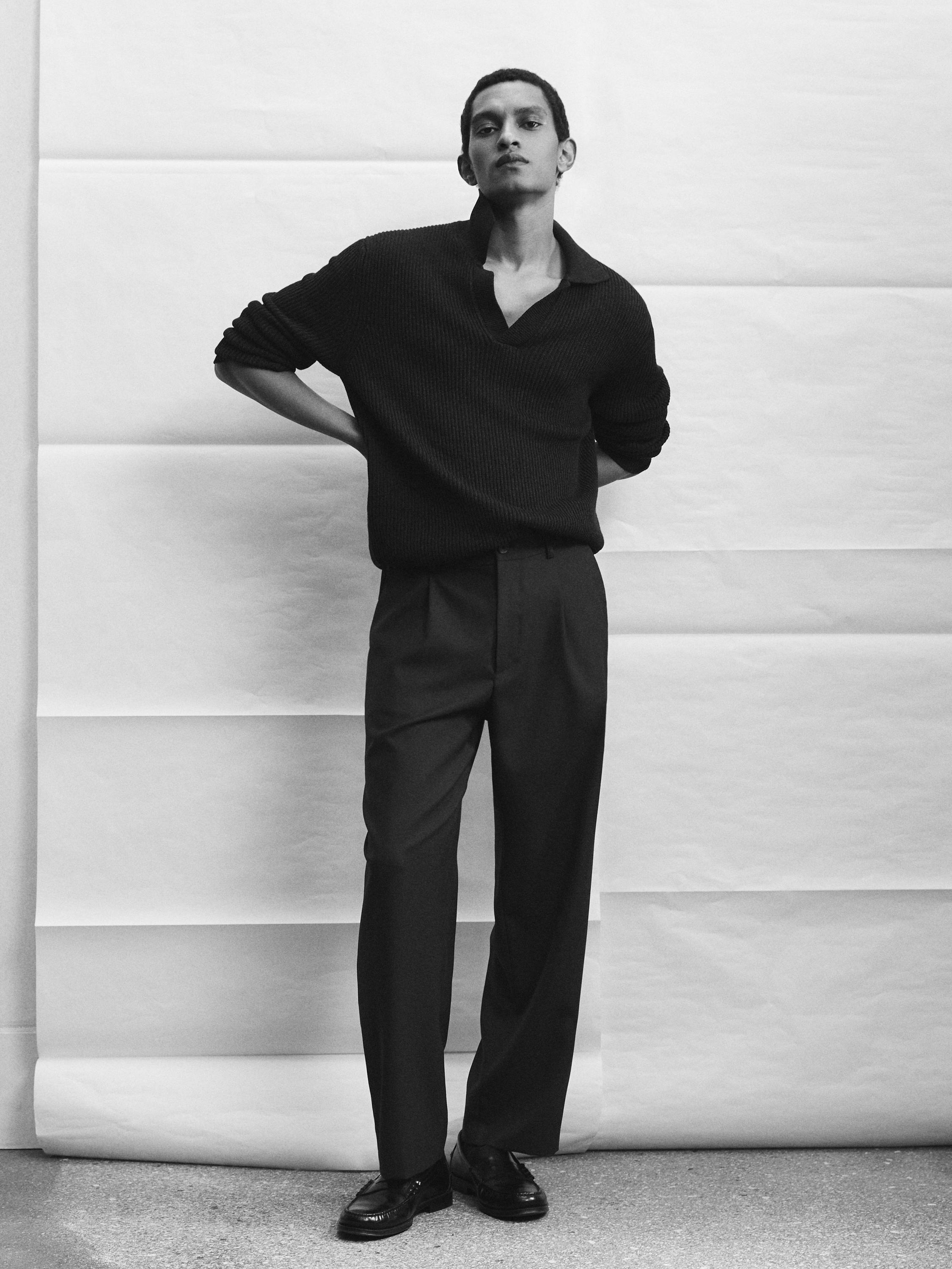 Açık yakalı siyah örgü süveter ve koyu renk düz kesim kumaş pantolon takımı.