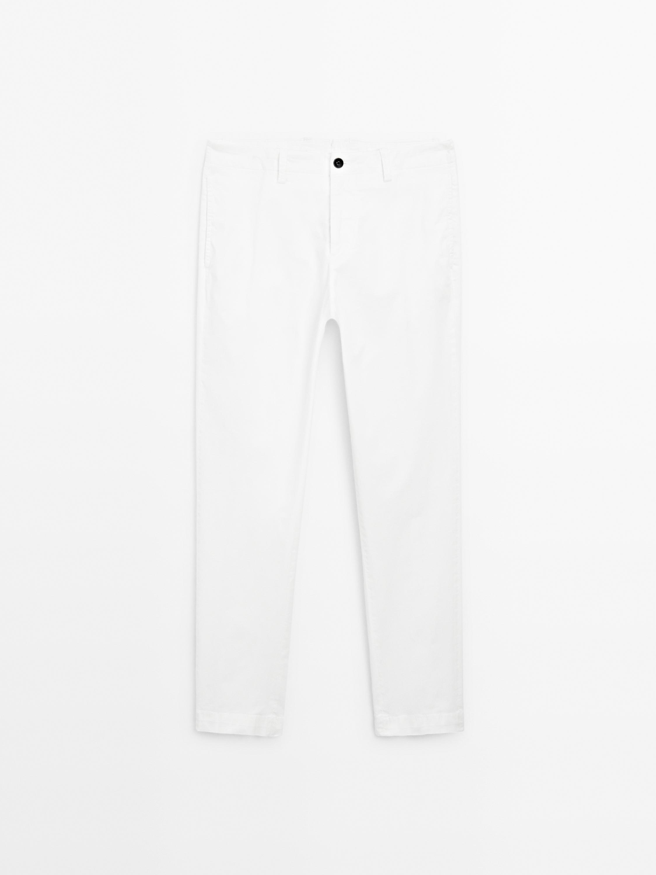 Front view of white slim fit pants with side pockets and black button.