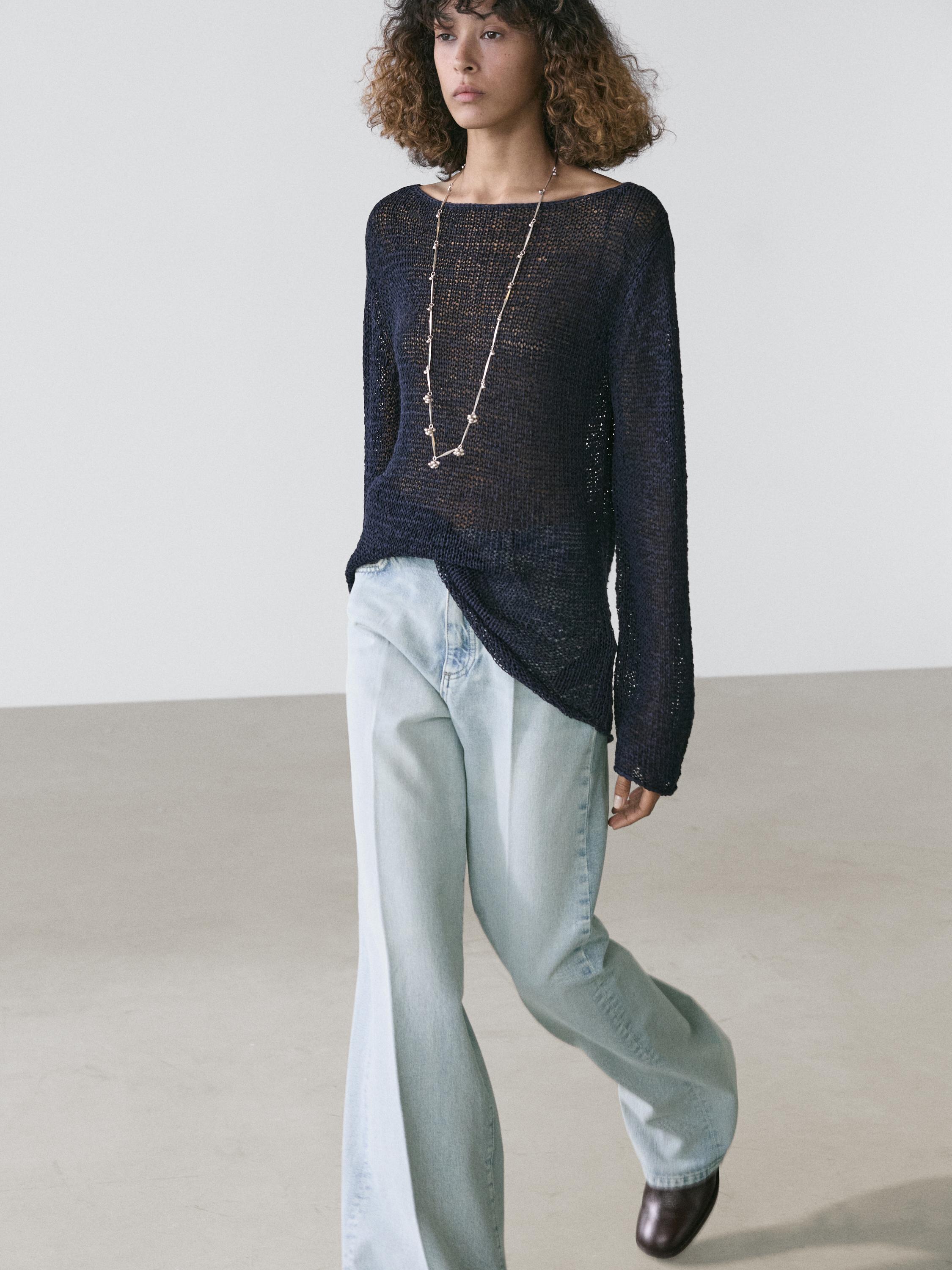 Conjunto de jeans palazzo azul claro de tiro alto y suéter negro de punto calado con cuello redondo.