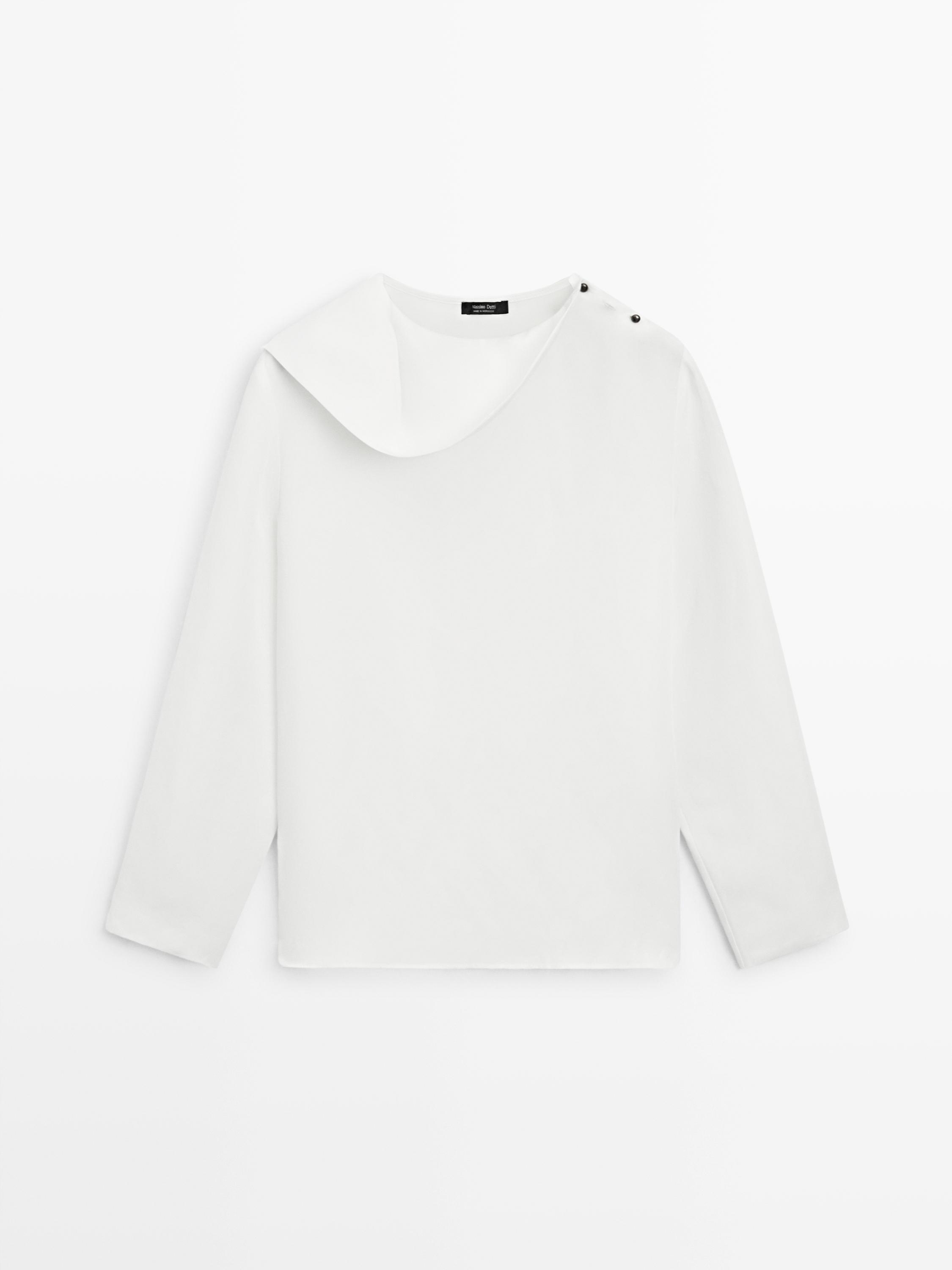 Вид спереду вільної білої сорочки з рюшами, ґудзиками на плечі та асиметричним коміром.