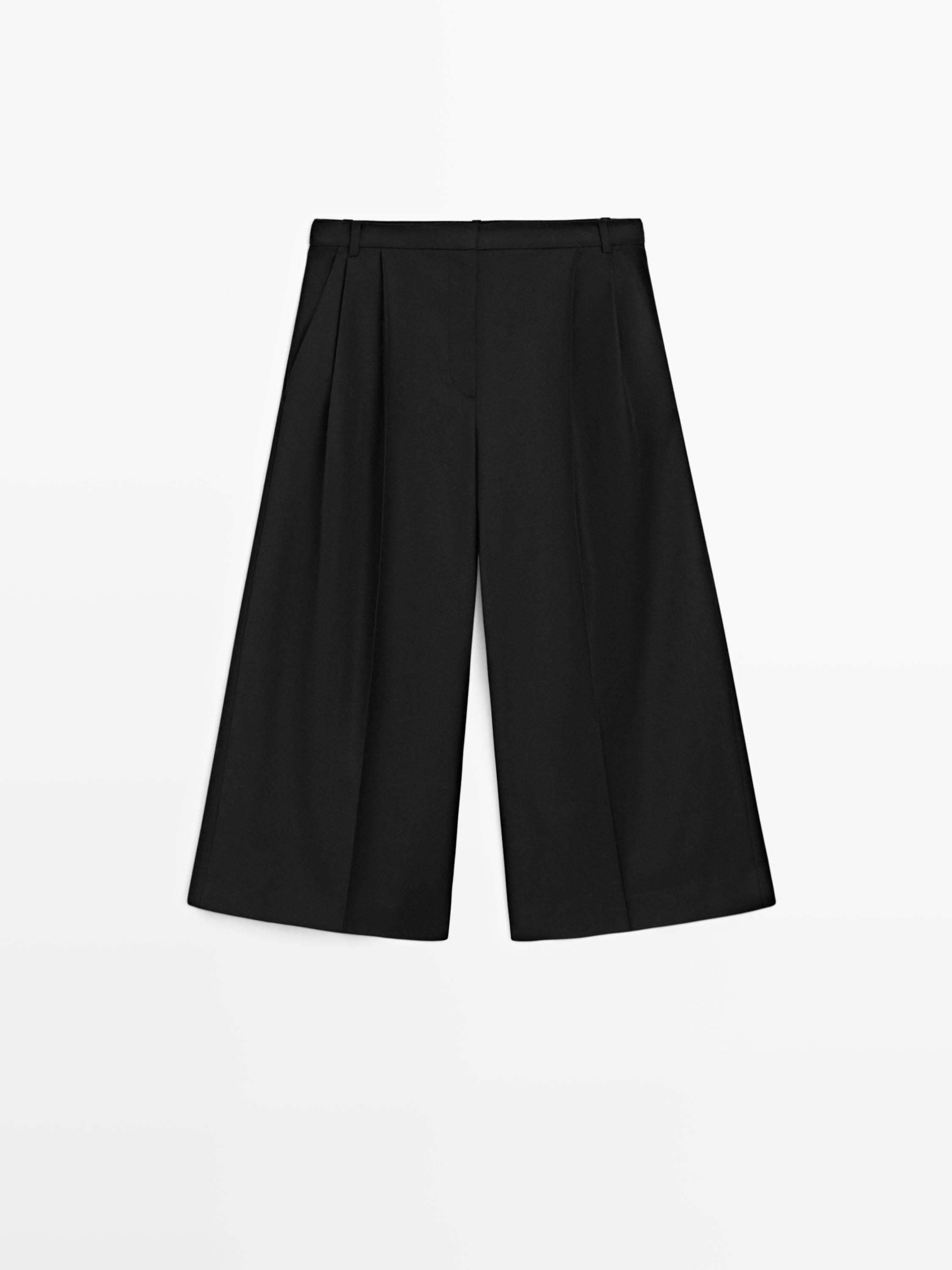 Front view of long black Bermuda shorts with pleats and a waistband with belt loops.