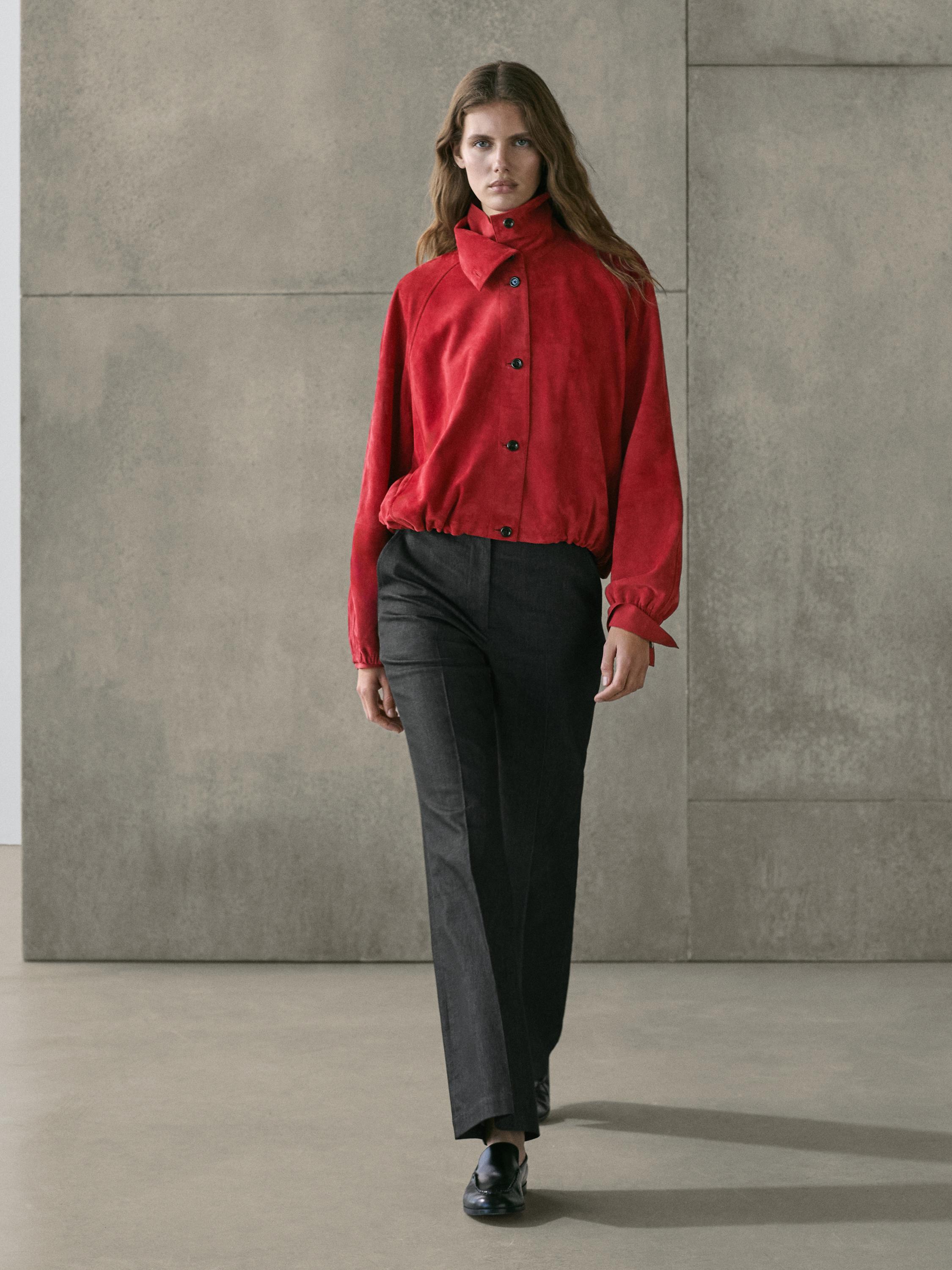 Комплект из красной куртки-бомбера на пуговицах с высоким воротником, прямых черных брюк и черных туфель.