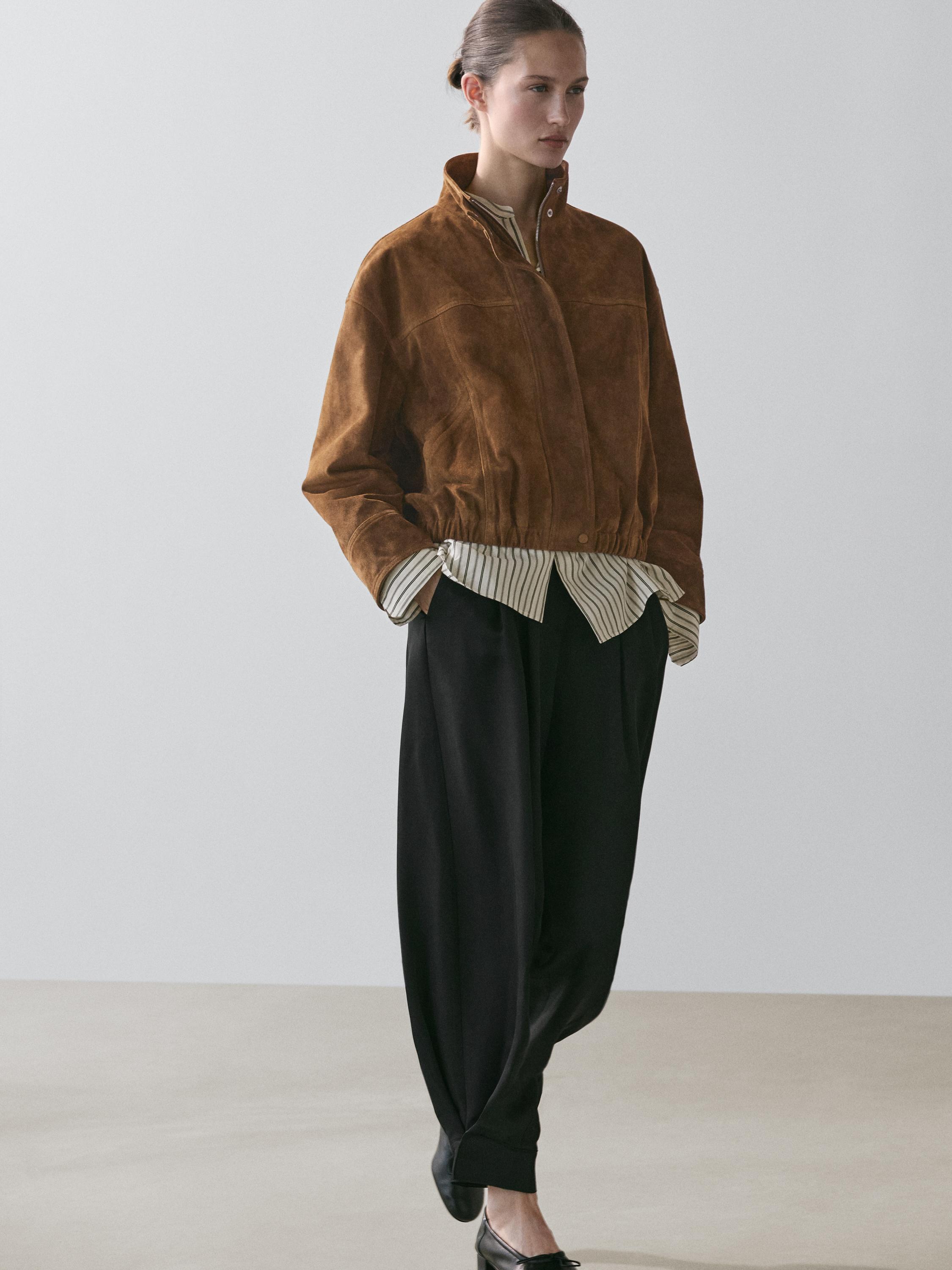 طقم جاكيت بومبر جملي بسحاب وبنطلون أسود فضفاض. قميص مخطط ظاهر عند الحافة.