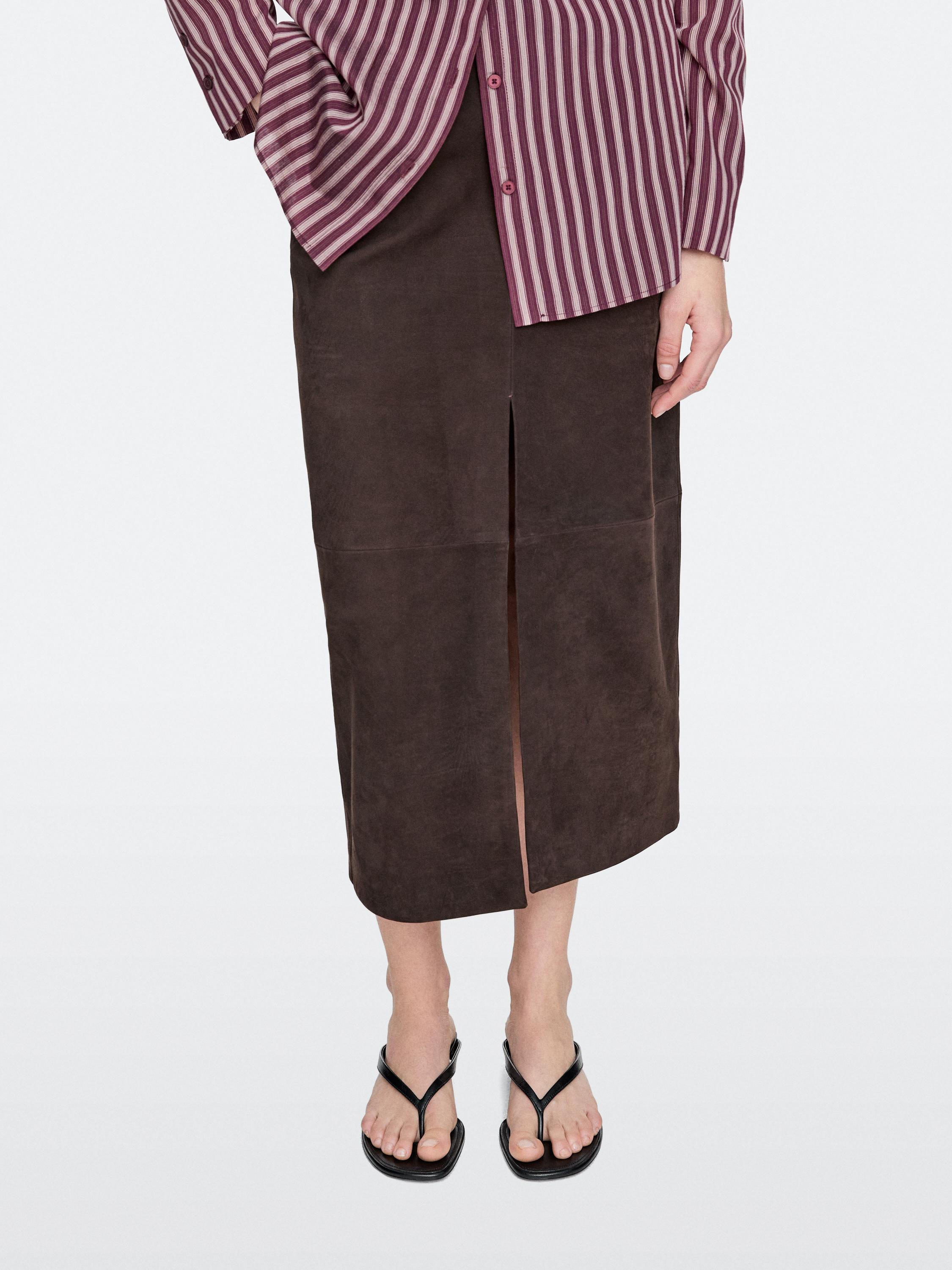Ensemble composé de sandales noires à talon moyen, d'une jupe marron fendue sur le devant et d'une chemise à rayures verticales.