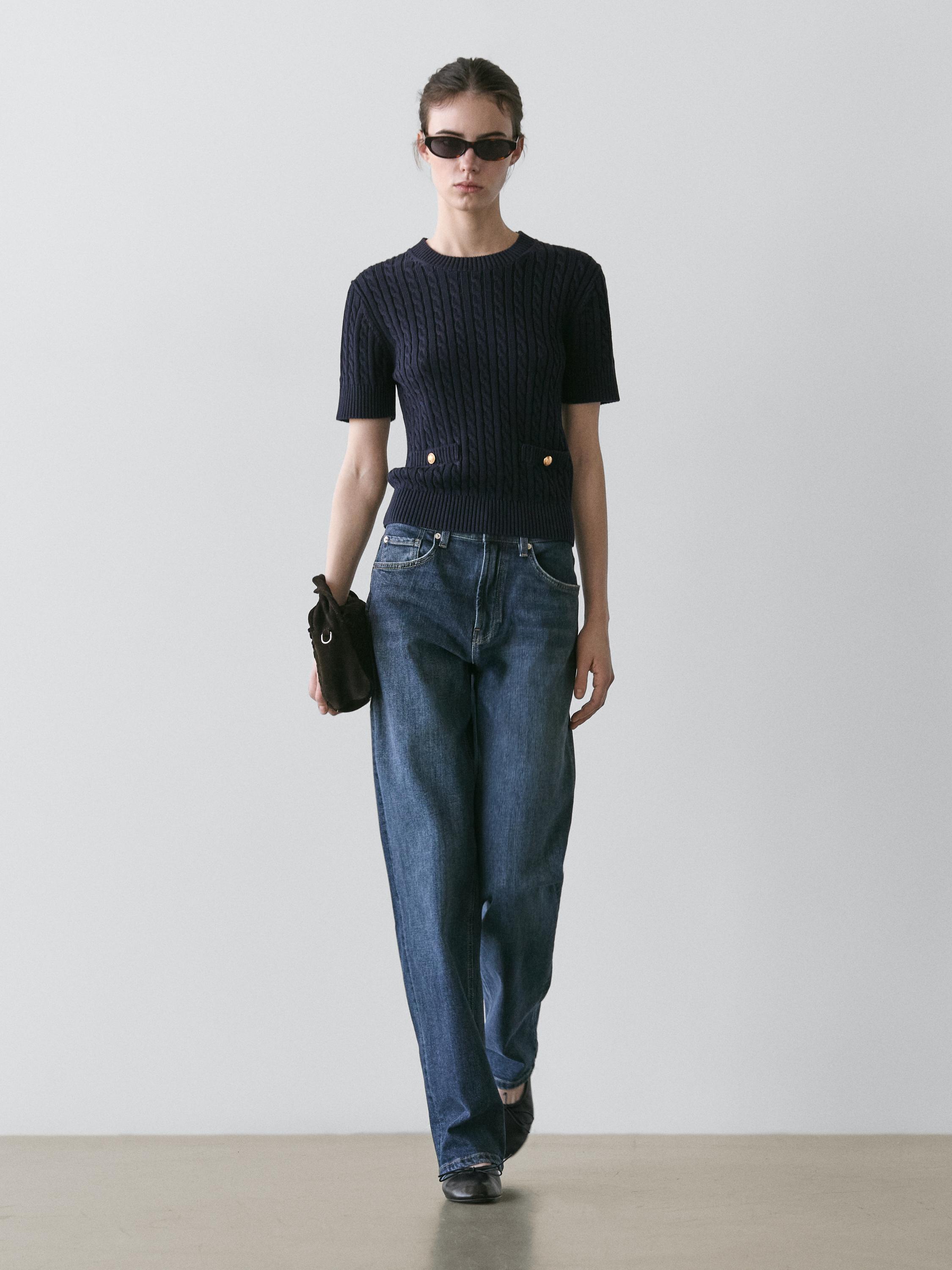 Komplet me pulovër marine me thurje kavoje me kopsa të arta dhe xhinse blu me prerje të drejtë.