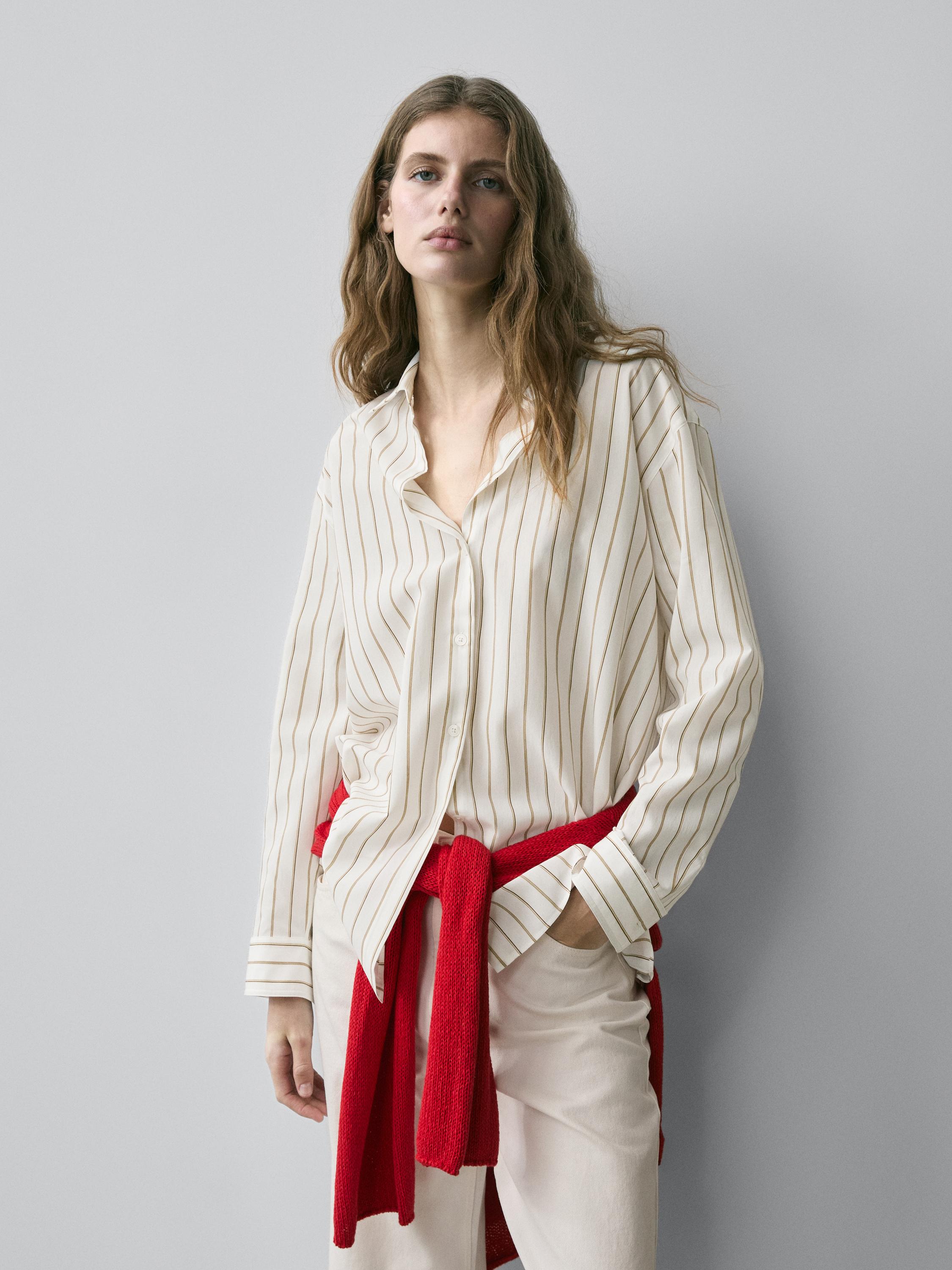 Komplet me këmishë të bardhë me vija trengjyrëshe dhe pantallona të çelëta. Pulovër i kuq i lidhur në bel.