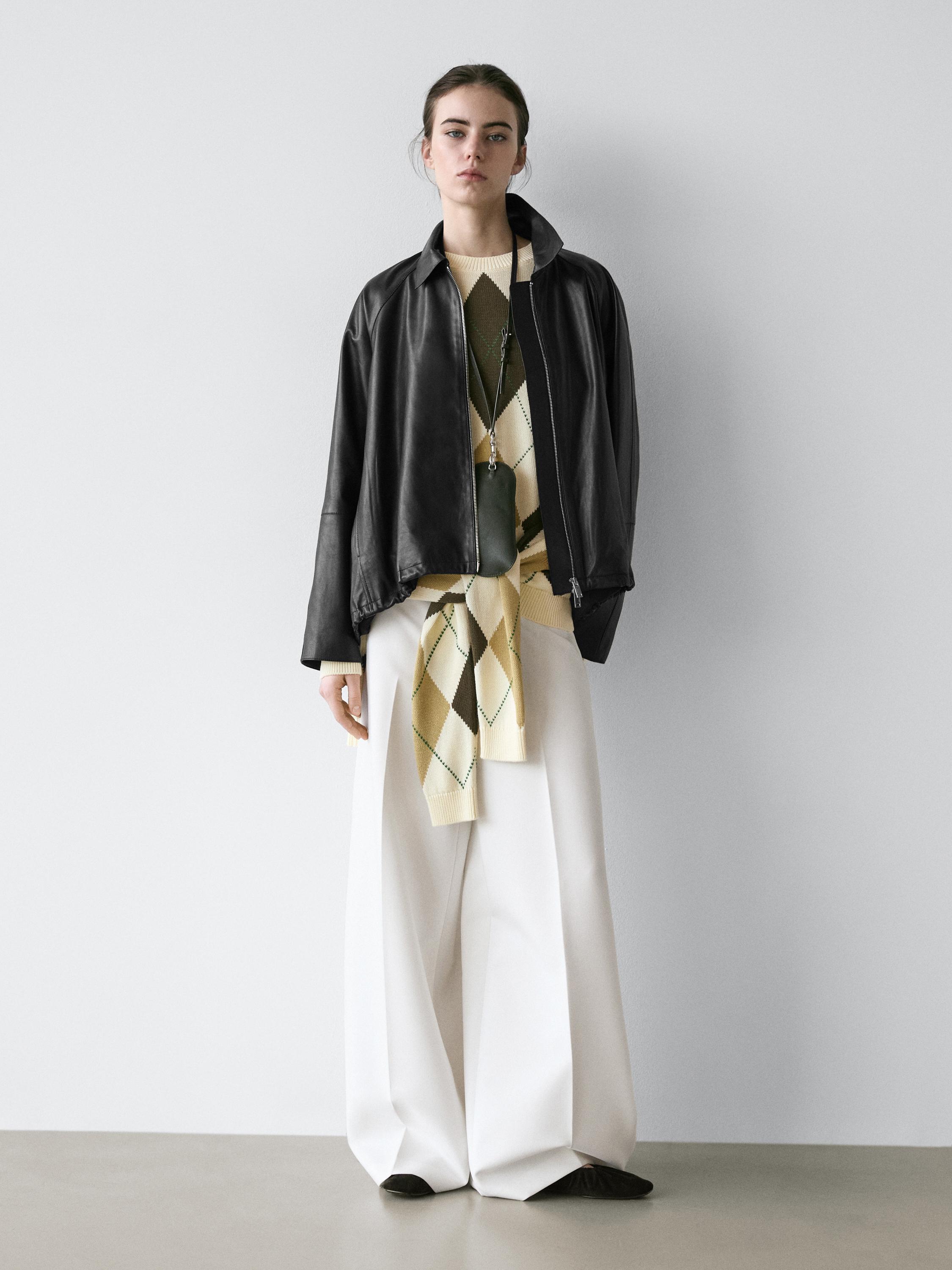 Ensemble composé d'une veste noire oversize, d'un pull à losanges beige et vert, d'un pantalon blanc ample et de chaussures noires.