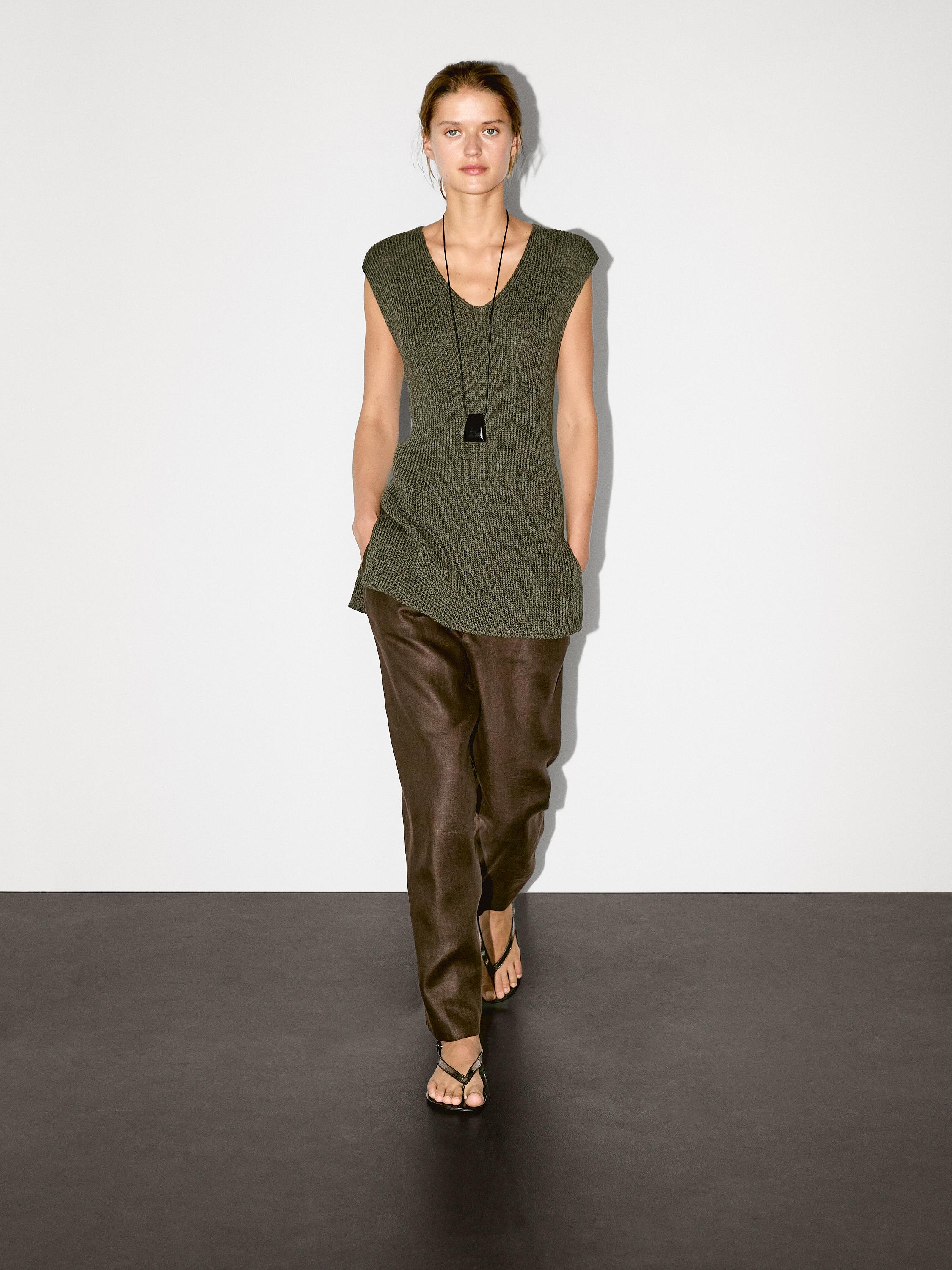 Ensemble composé d'un pull sans manches vert et d'un pantalon marron, avec des sandales. Col en V et poches latérales.