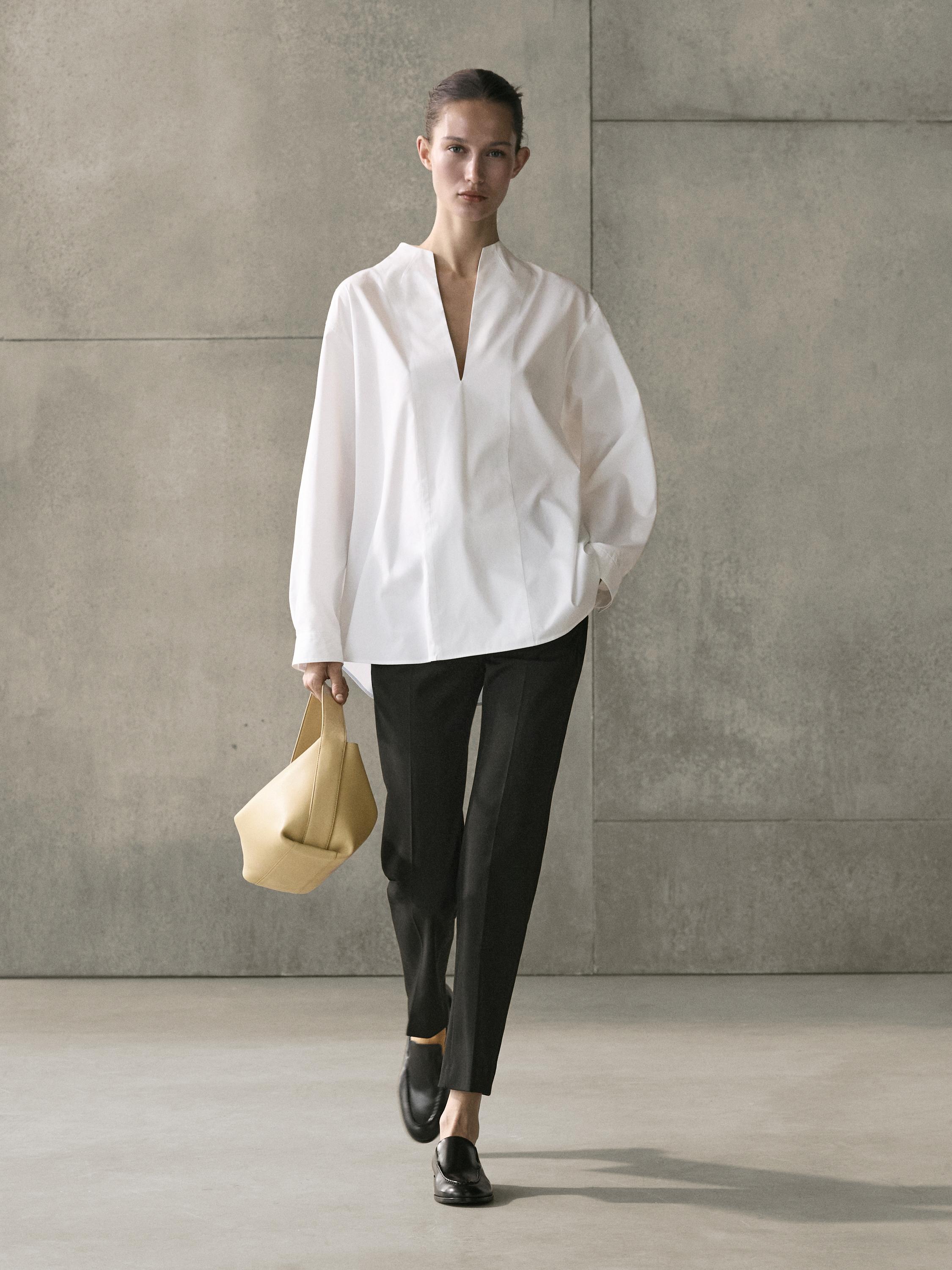 Open-collar white shirt and black straight-leg pants set. She's wearing a beige bag and black loafers.