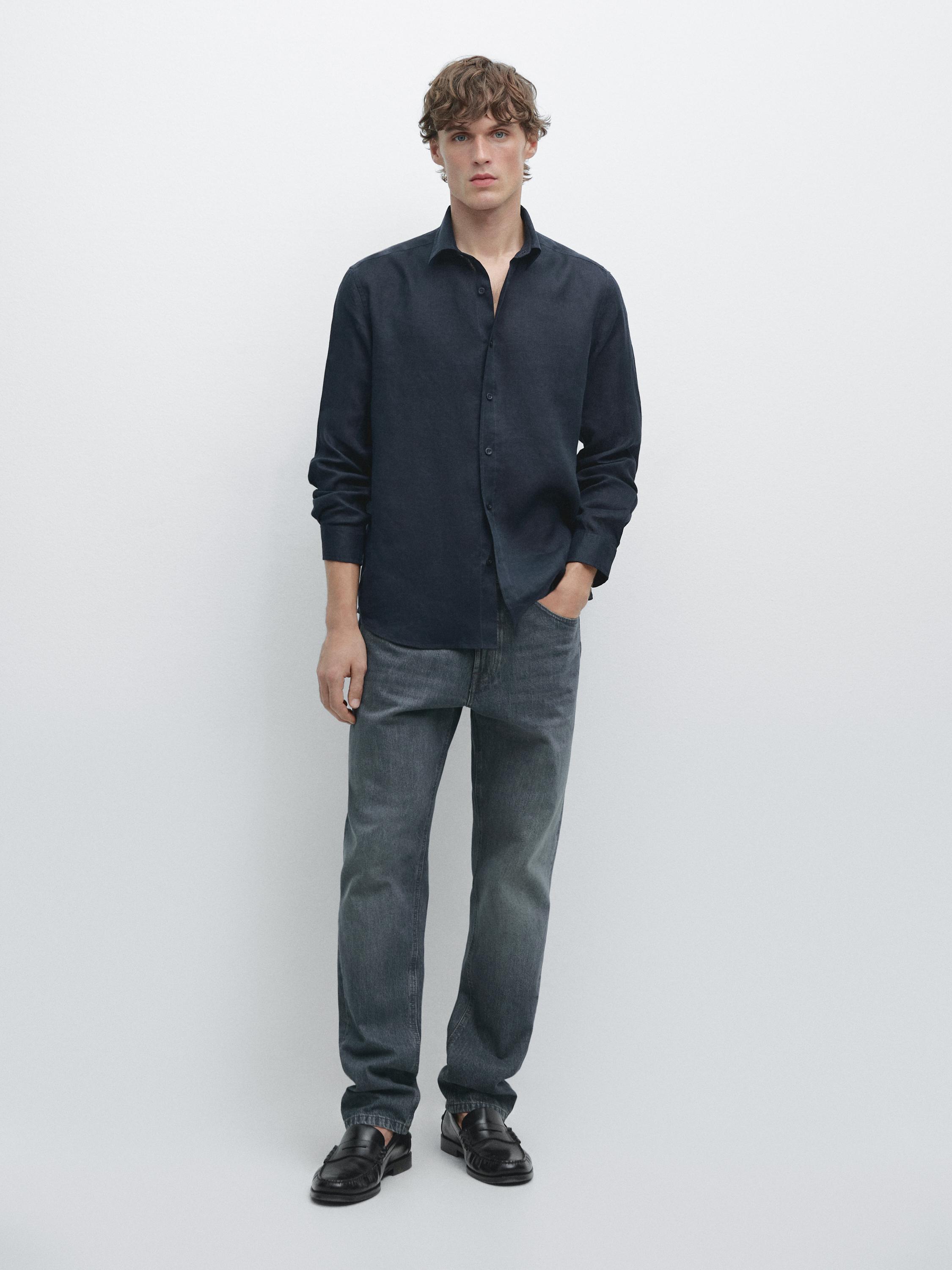 Completo di camicia blu scuro a maniche lunghe e pantaloni jeans grigi.