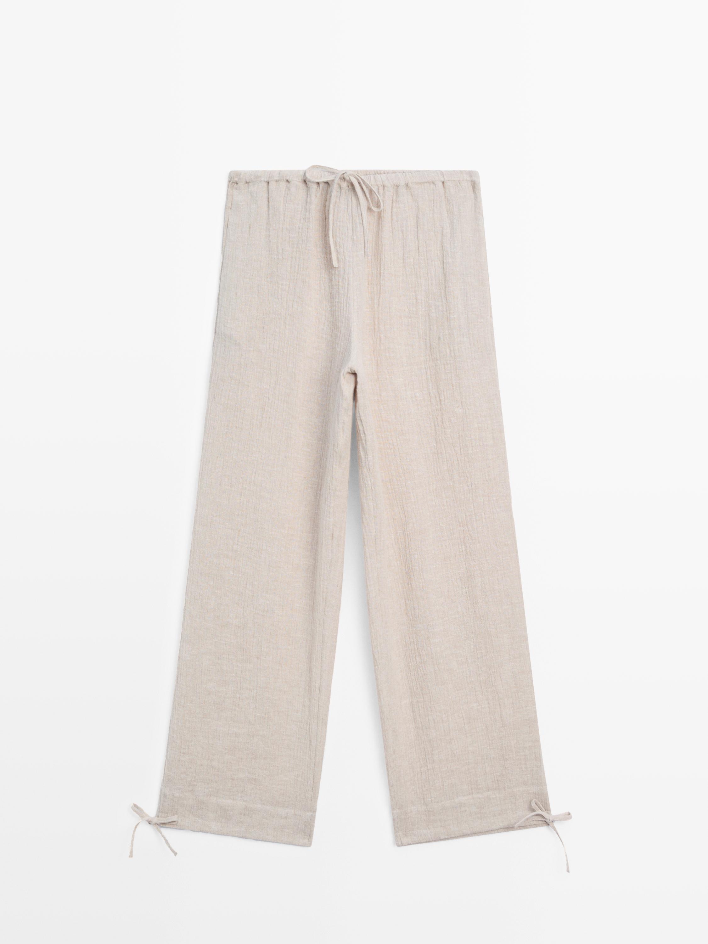 Vista frontal de pantalón arena con cintura elástica y cordón ajustable, pernera recta y lazos en los bajos.