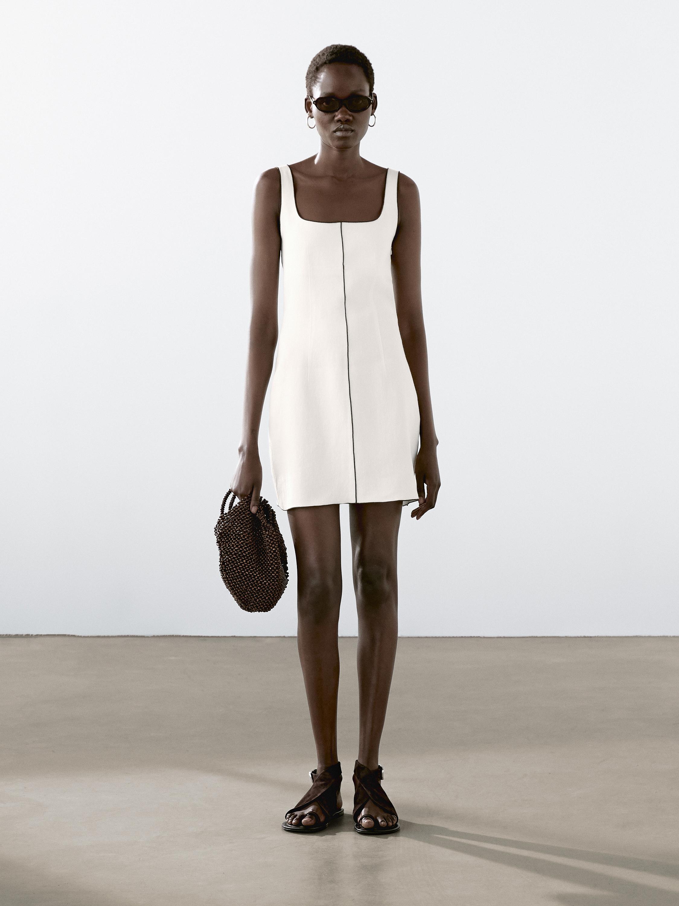 Ensemble comprenant une robe blanche sans manches avec une ligne centrale, des sandales noires et un sac à main marron.