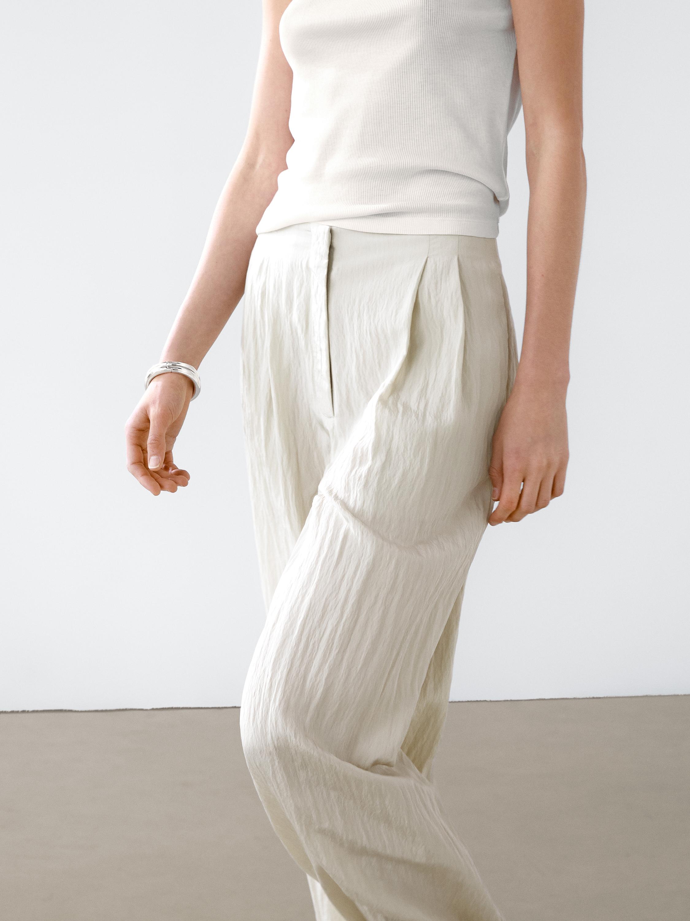 Plan moyen d'un pantalon technique à pinces de couleur claire et d'un débardeur.