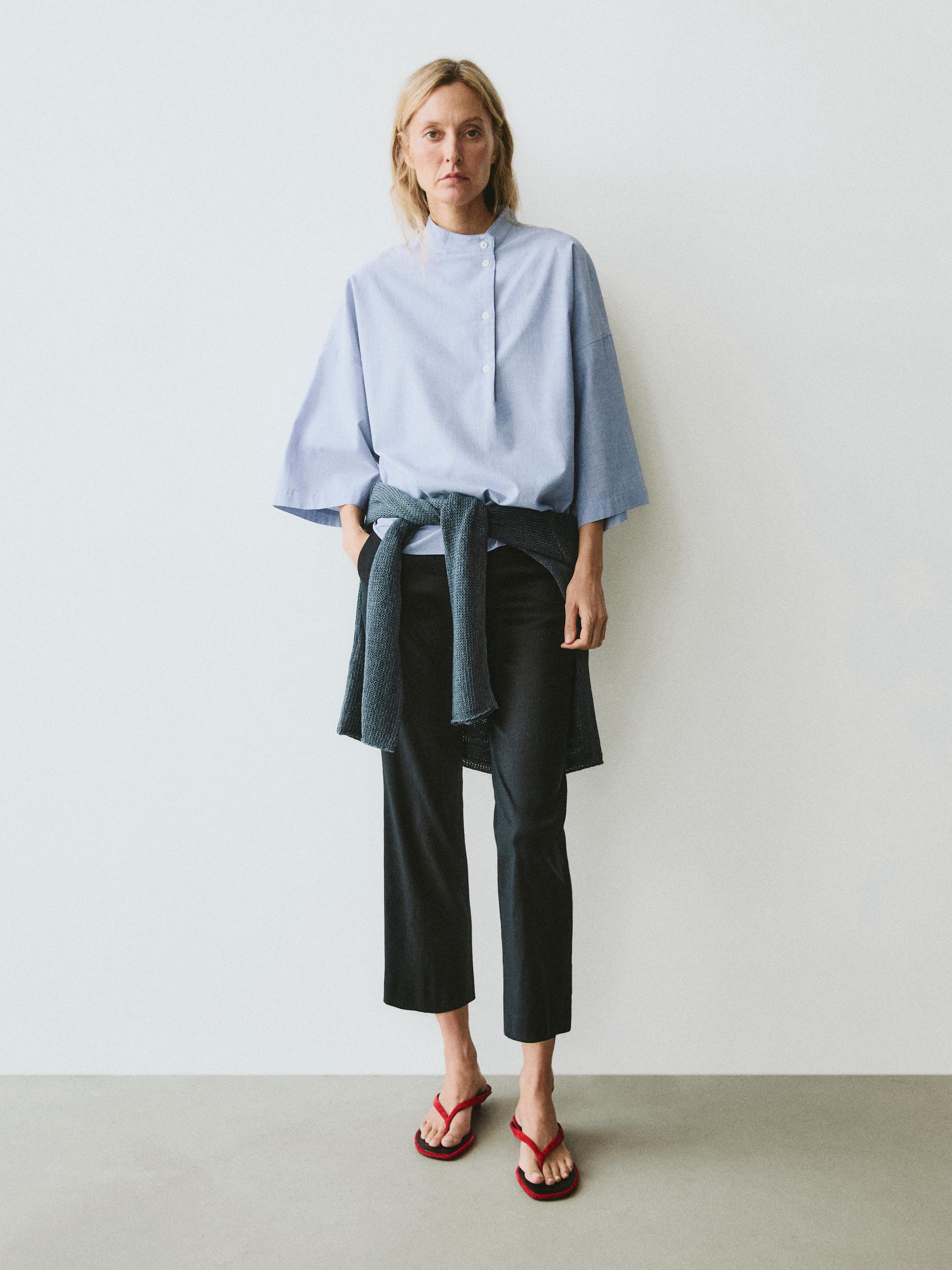 Conjunto de blusa azul de mezclilla fluida con cuello abotonado y mangas amplias, pantalones negros y sandalias rojas.