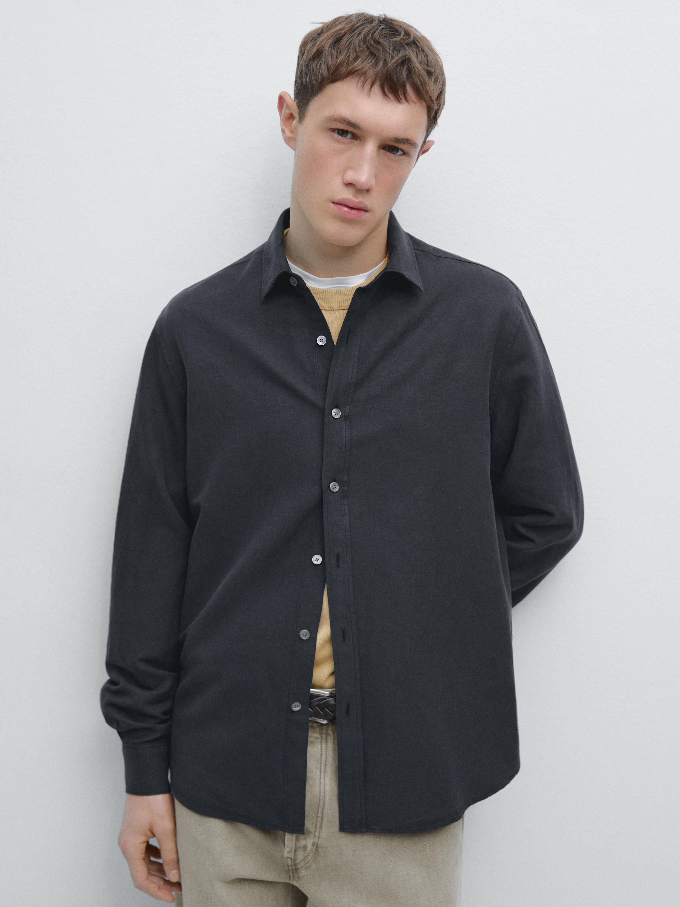 Ensemble composé d'une chemise bleu marine à manches longues boutonnée et à col classique, portée sur un t-shirt beige, et d'un pantalon beige.