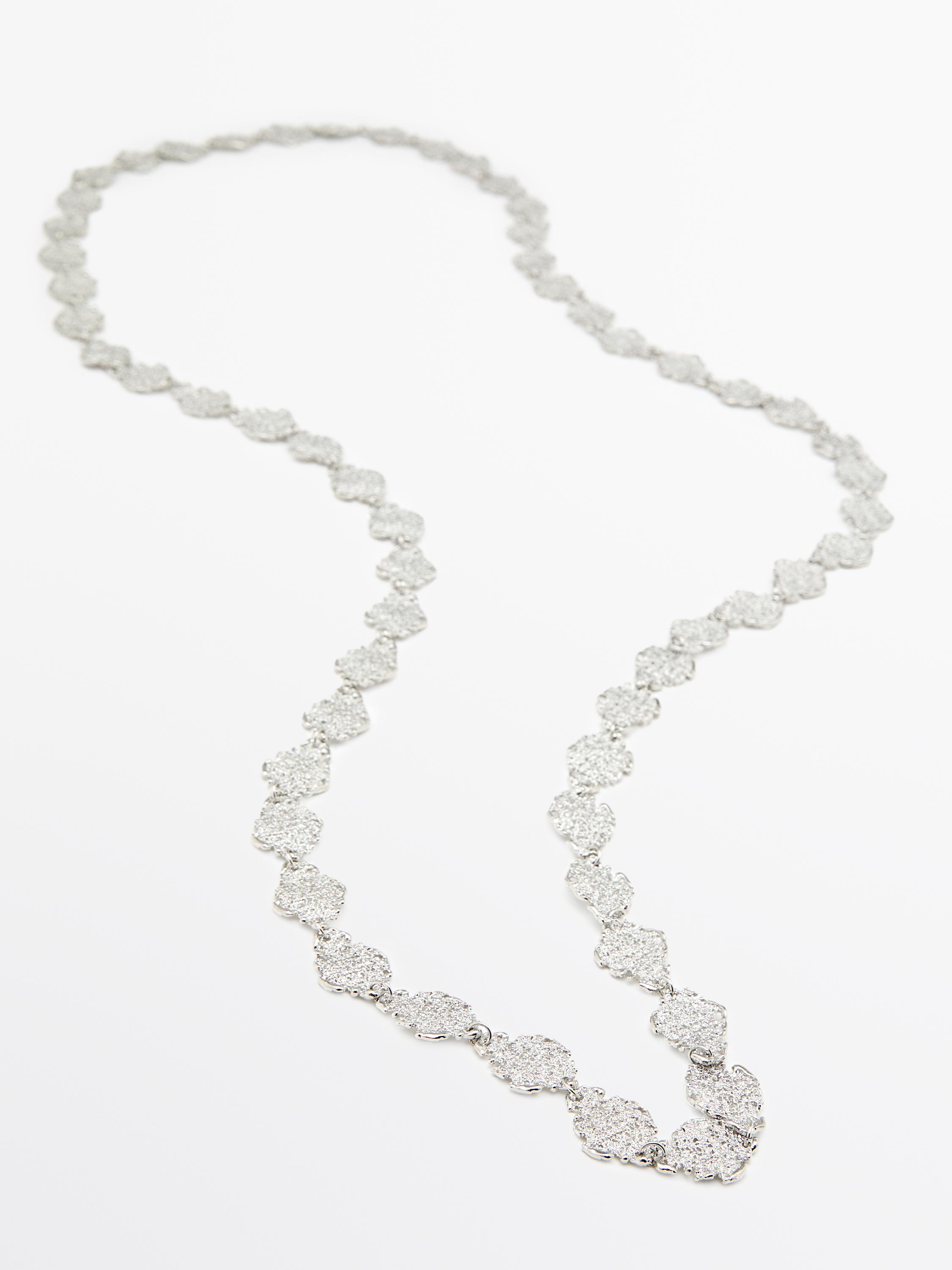 Колье-бижутерия серебристого цвета с текстурированными звеньями в форме листьев.