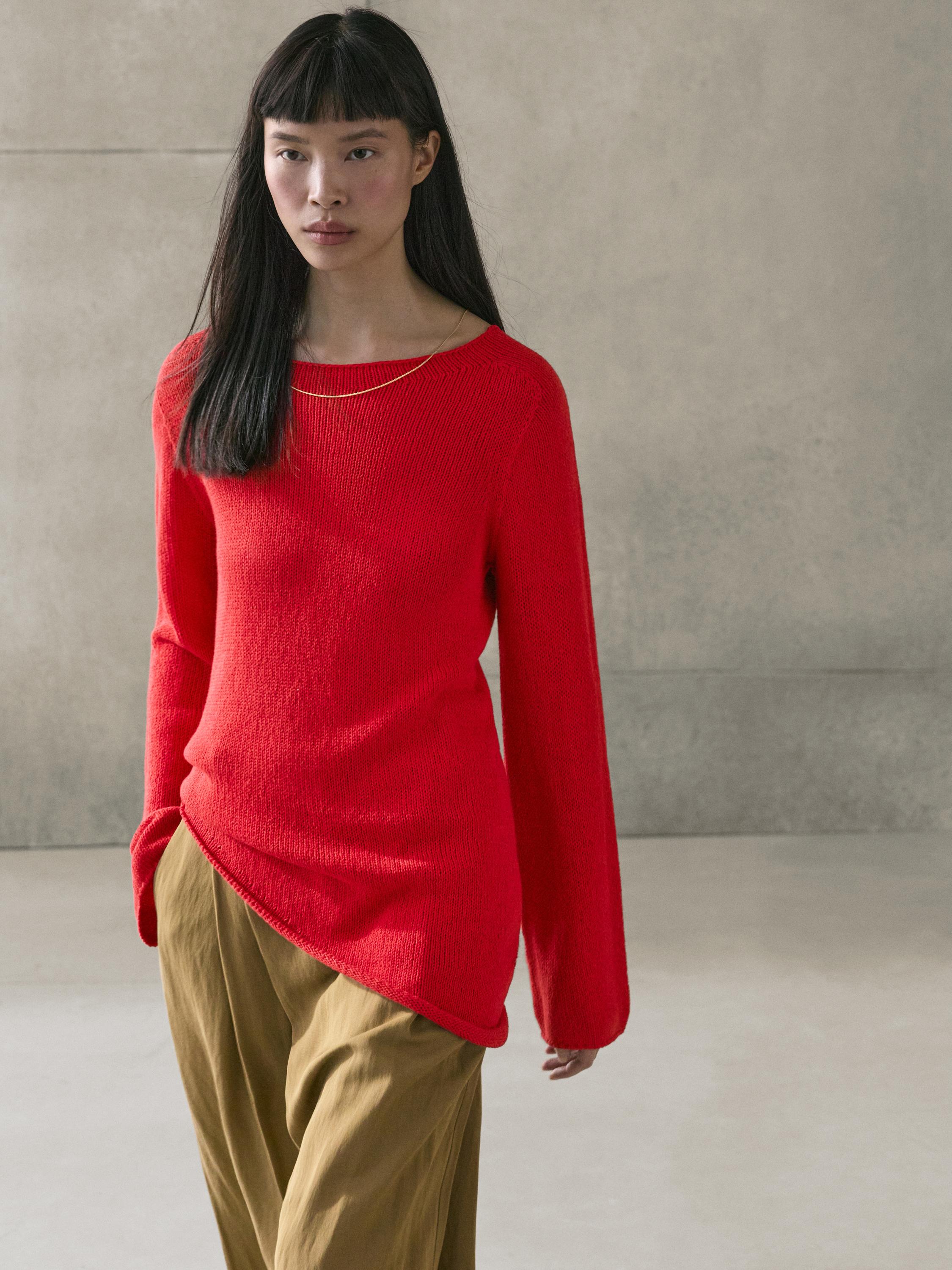 Red knit sweater set with an asymmetrical cut and loose beige pants.