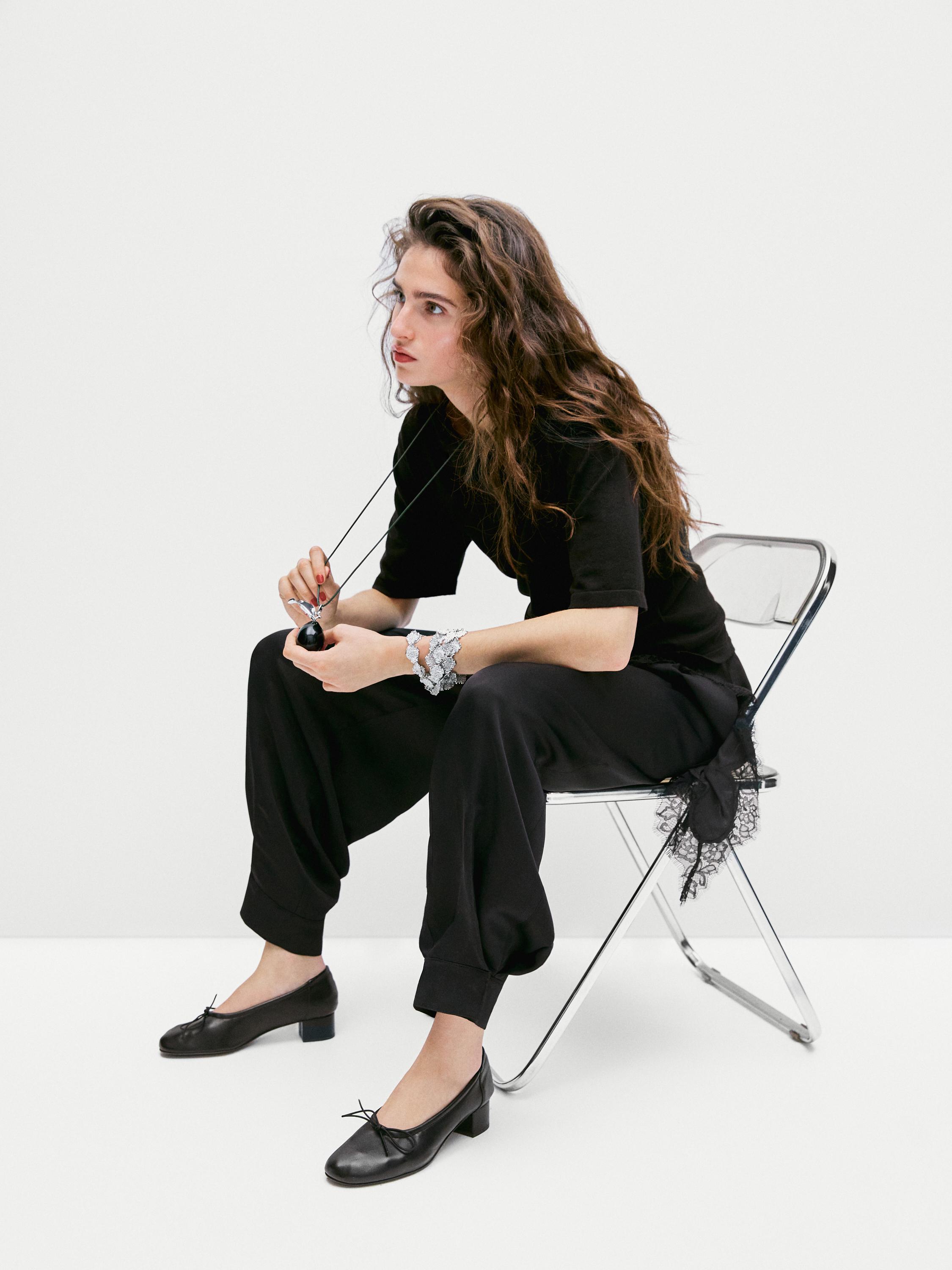 Ensemble composé d'un pendentif argenté, d'un t-shirt noir à manches courtes, d'un pantalon noir ample et de chaussures noires à nœud.