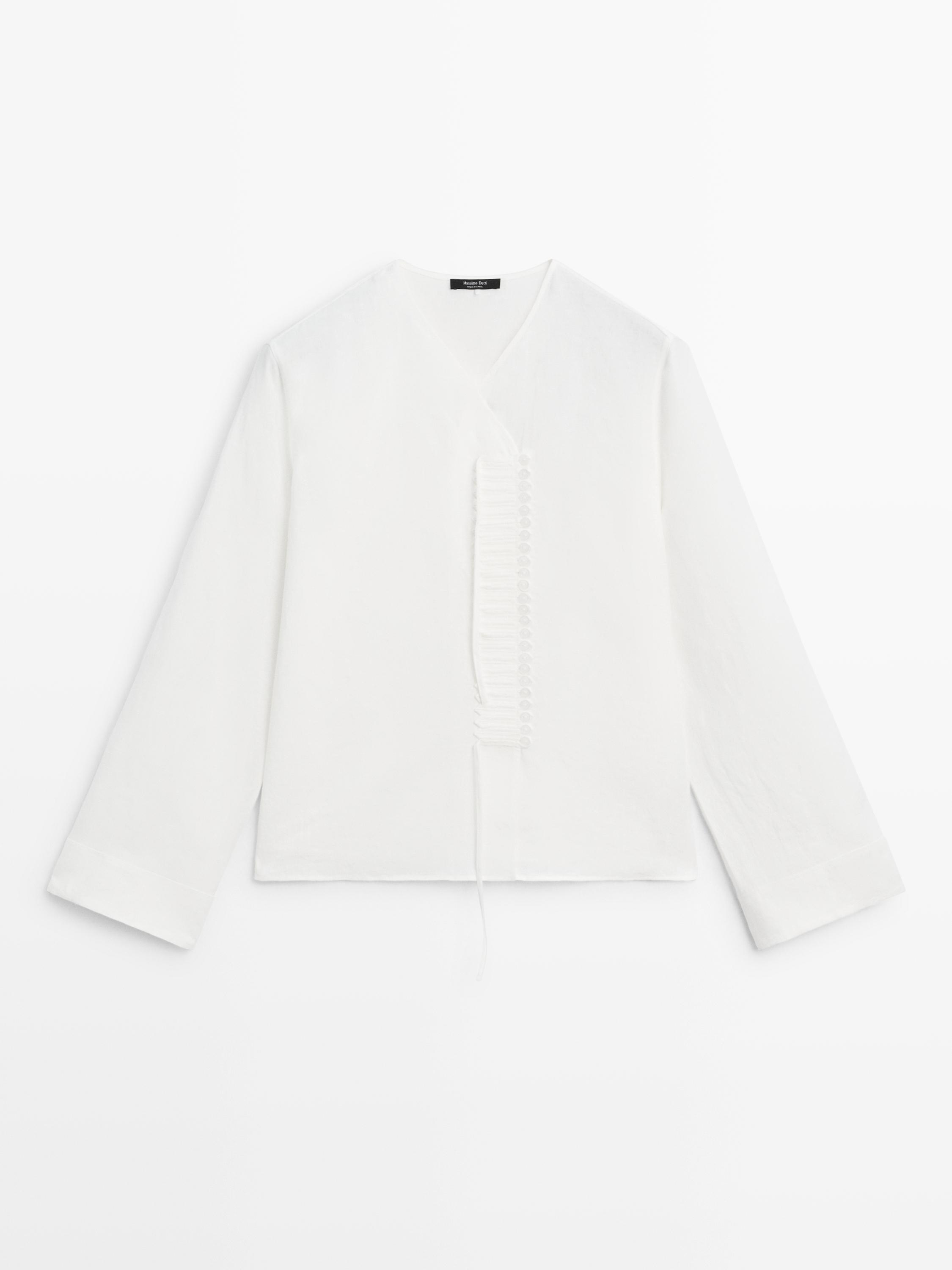 Vista frontal de camisa blanca con cuello en V y botonadura central decorativa. Mangas largas y corte recto.