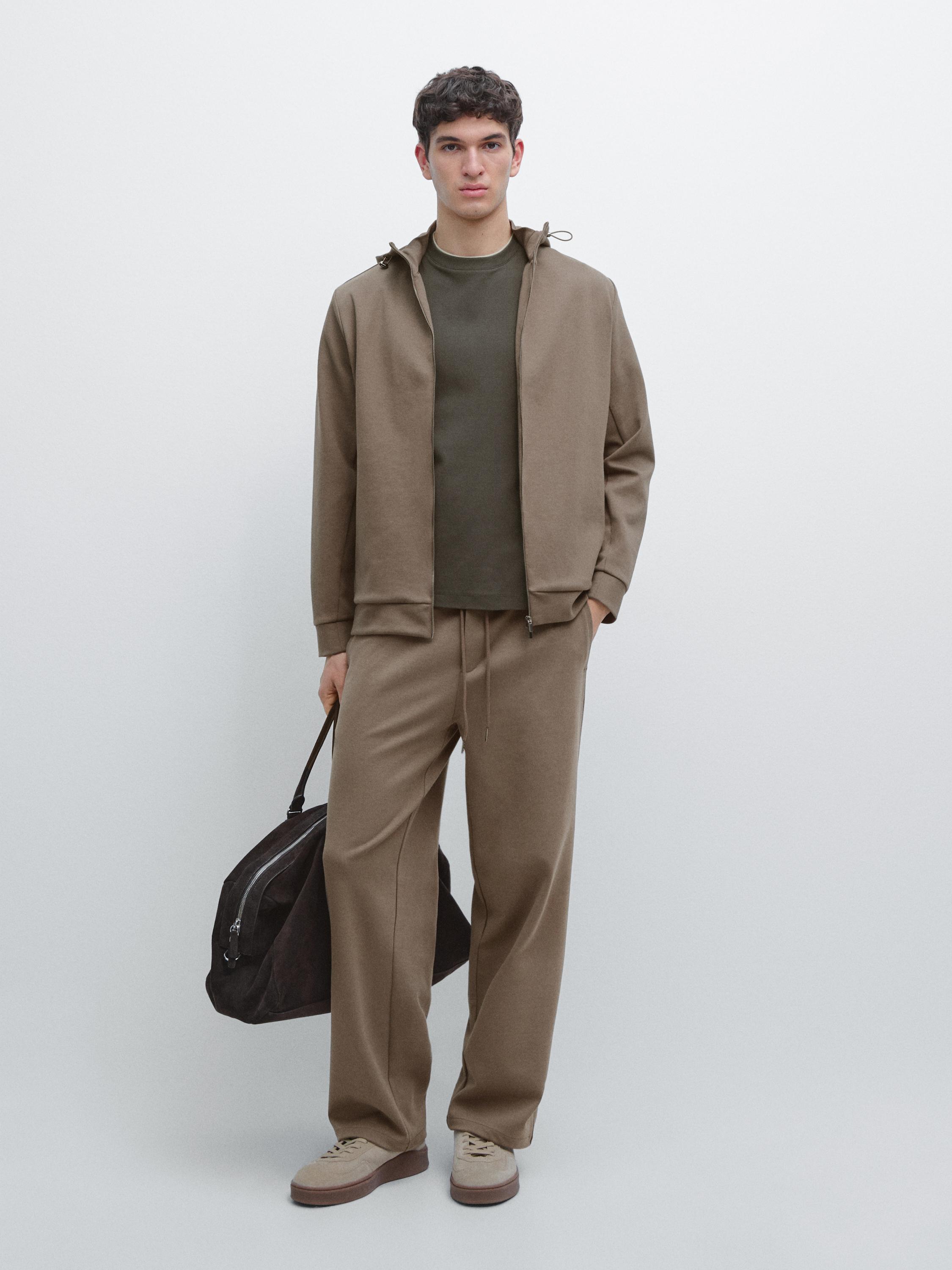 Ensemble veste et pantalon kaki, t-shirt vert, baskets beiges et sac à main foncé.