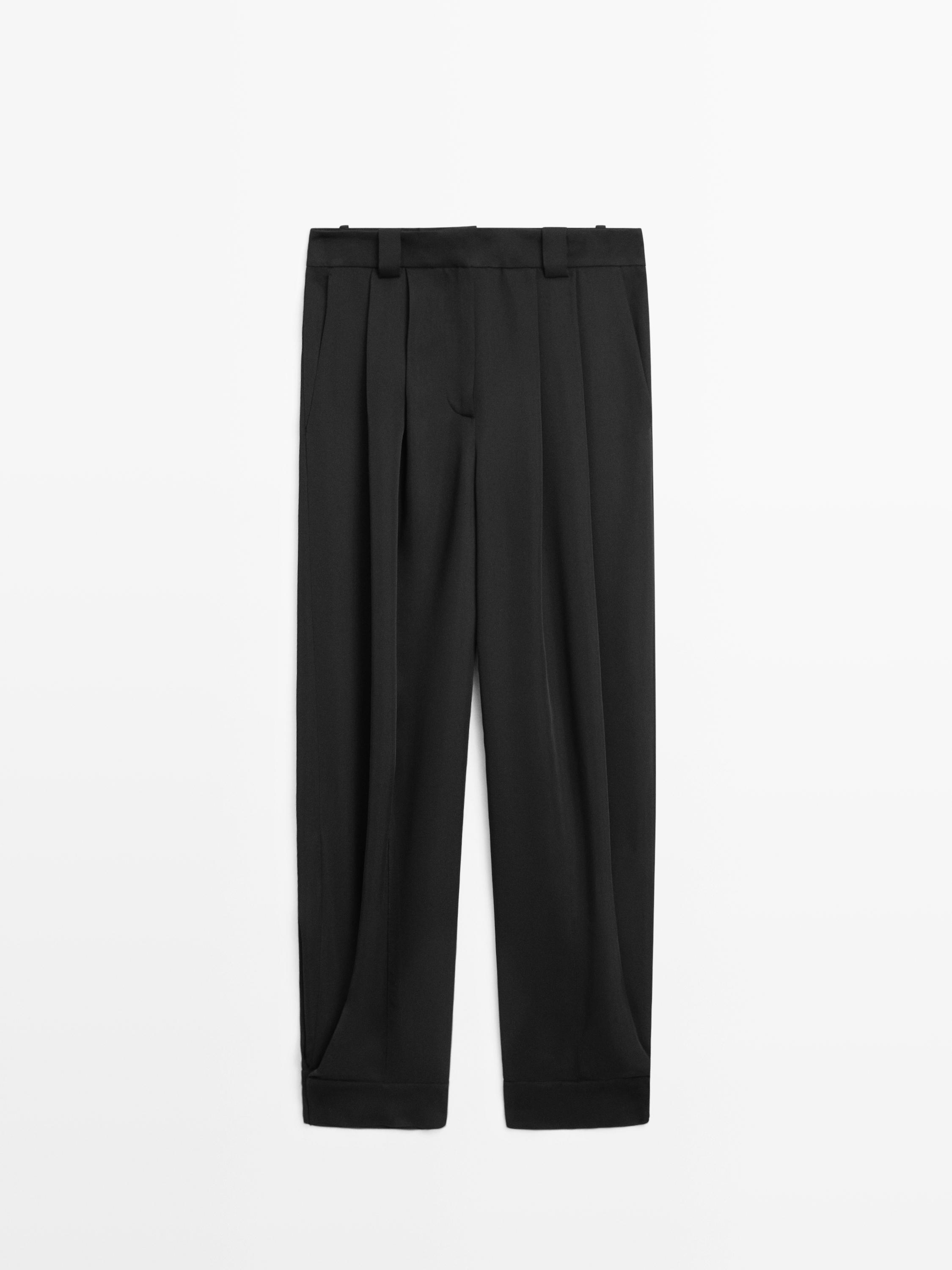 Vista frontal de pantalón bombacho negro con pliegues y trabillas para cinturón.