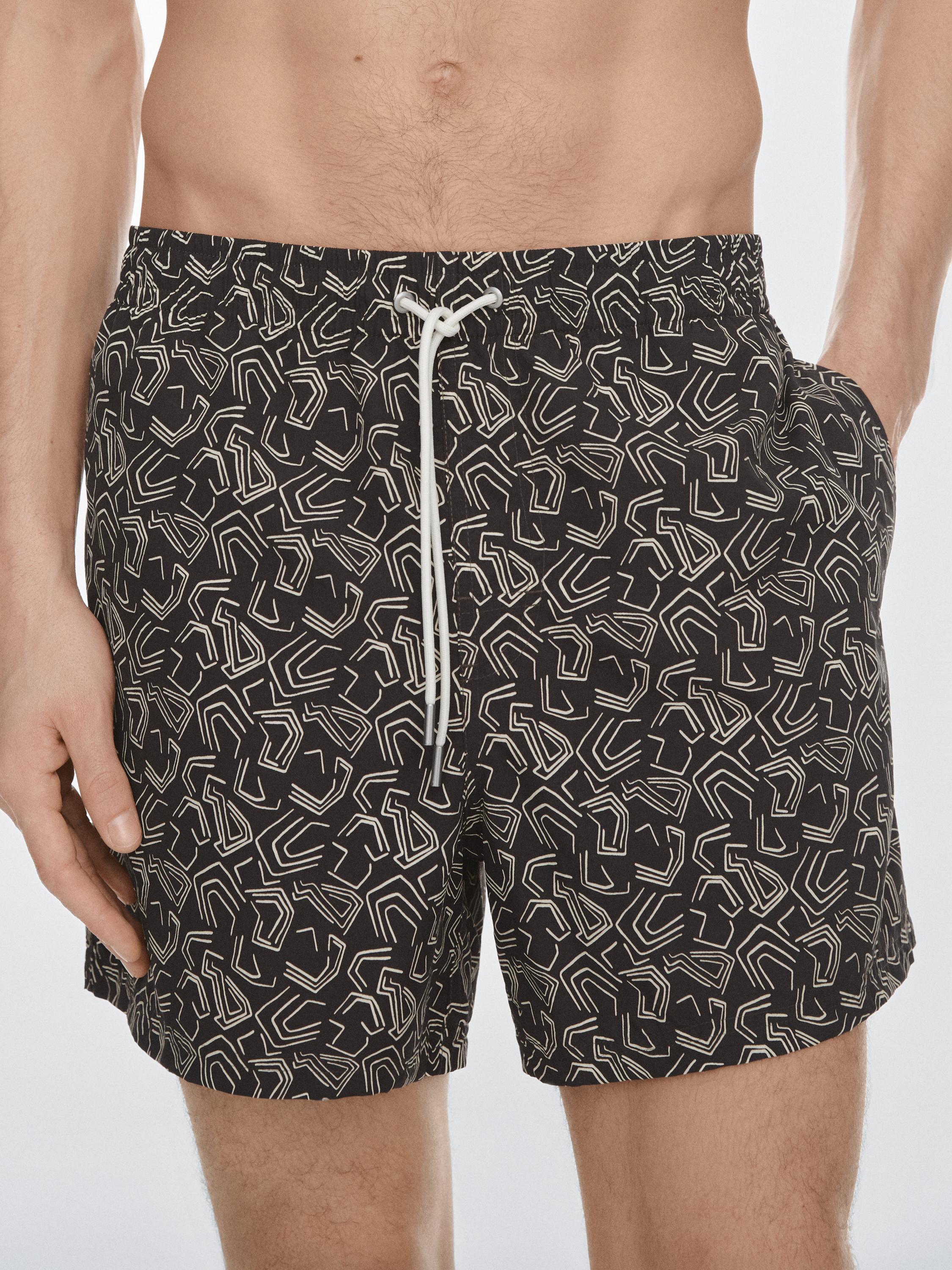 "Halbaufnahme eines braunen Badeanzugs mit abstraktem Muster und weißem Kordelzug, sichtbare Seitentaschen."