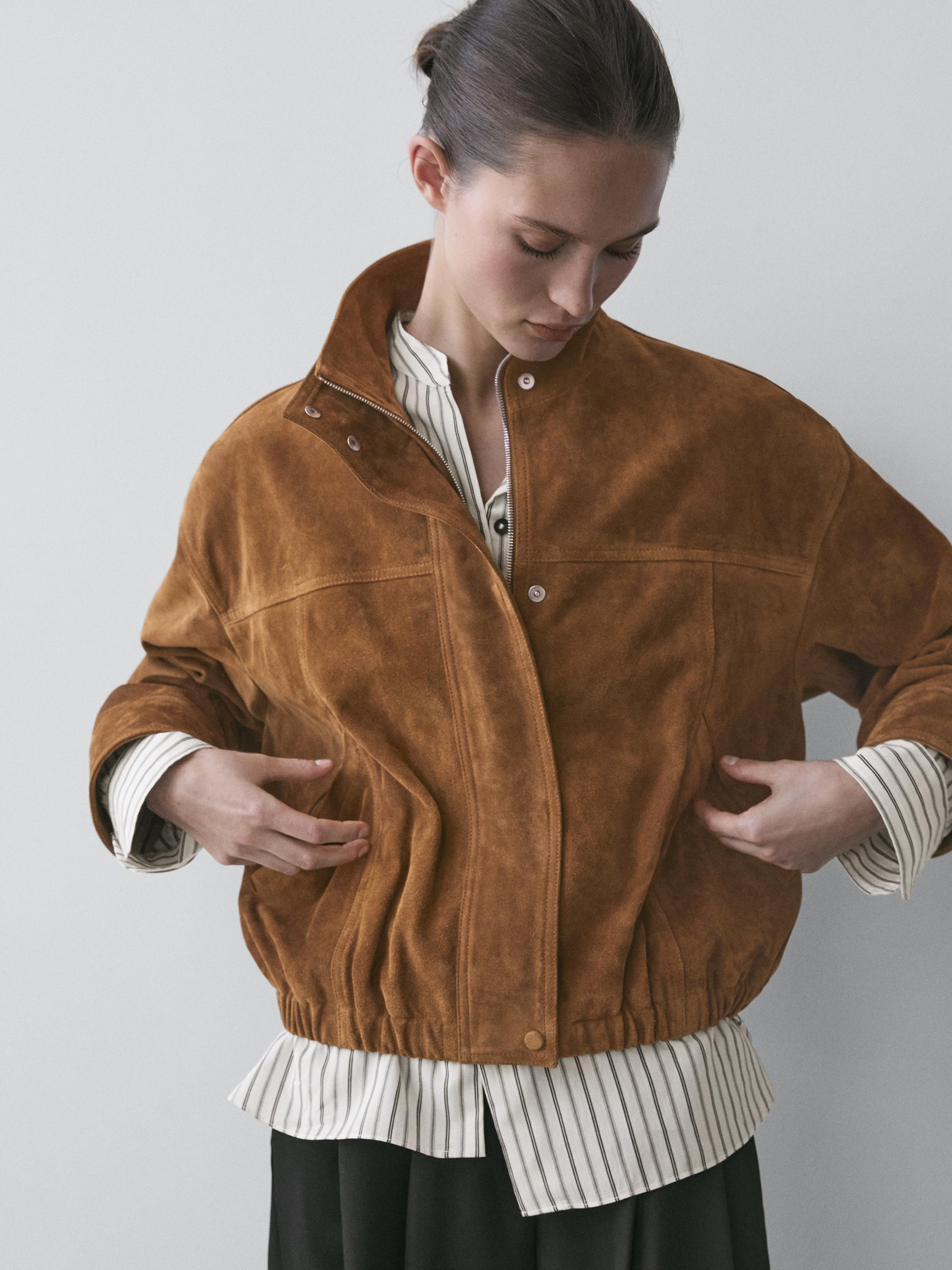 Zbliżenie kurtki bomber camel z zapięciem na guziki i zamkiem błyskawicznym, bocznymi kieszeniami i elastycznym ściągaczem.