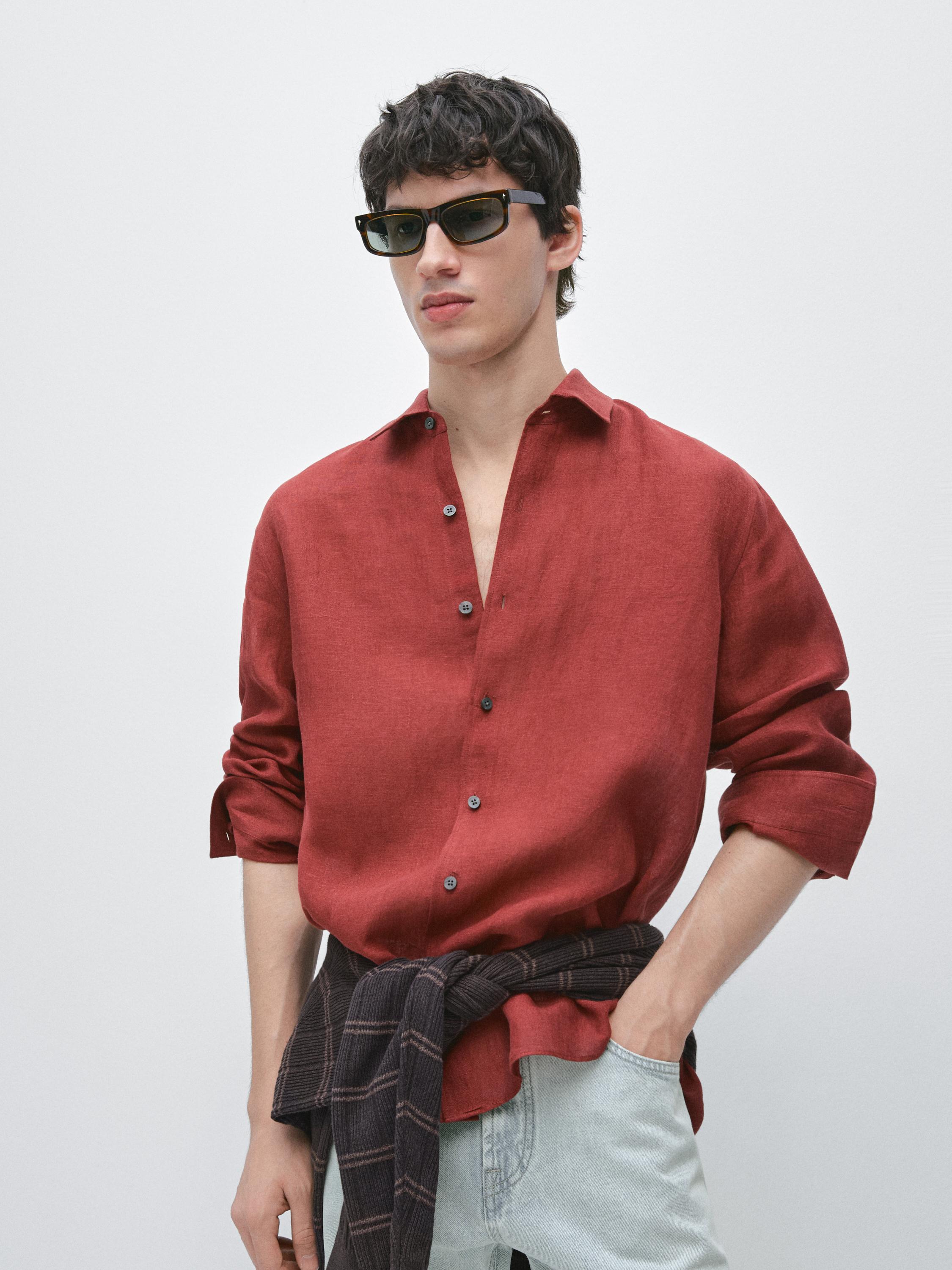 Langärmeliges rotes Hemd mit dunklen Knöpfen und heller Hose. Dunkler Pullover um die Taille gebunden.