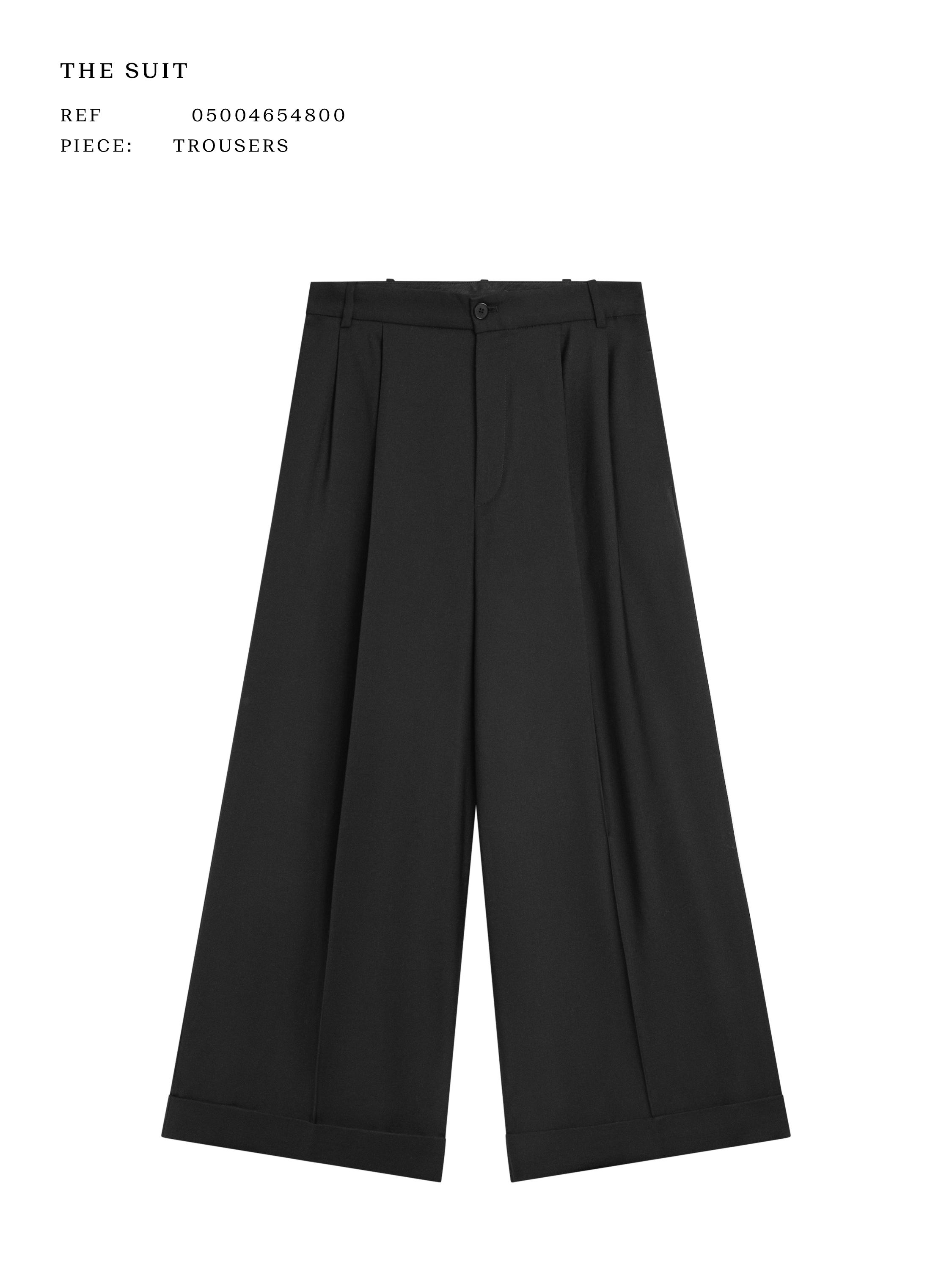 Front view of flowing black trousers with pleats, wide leg, and button closure. Visible text: "THE SUIT", "REF 05004654800", "PIECE: TROUSERS".
