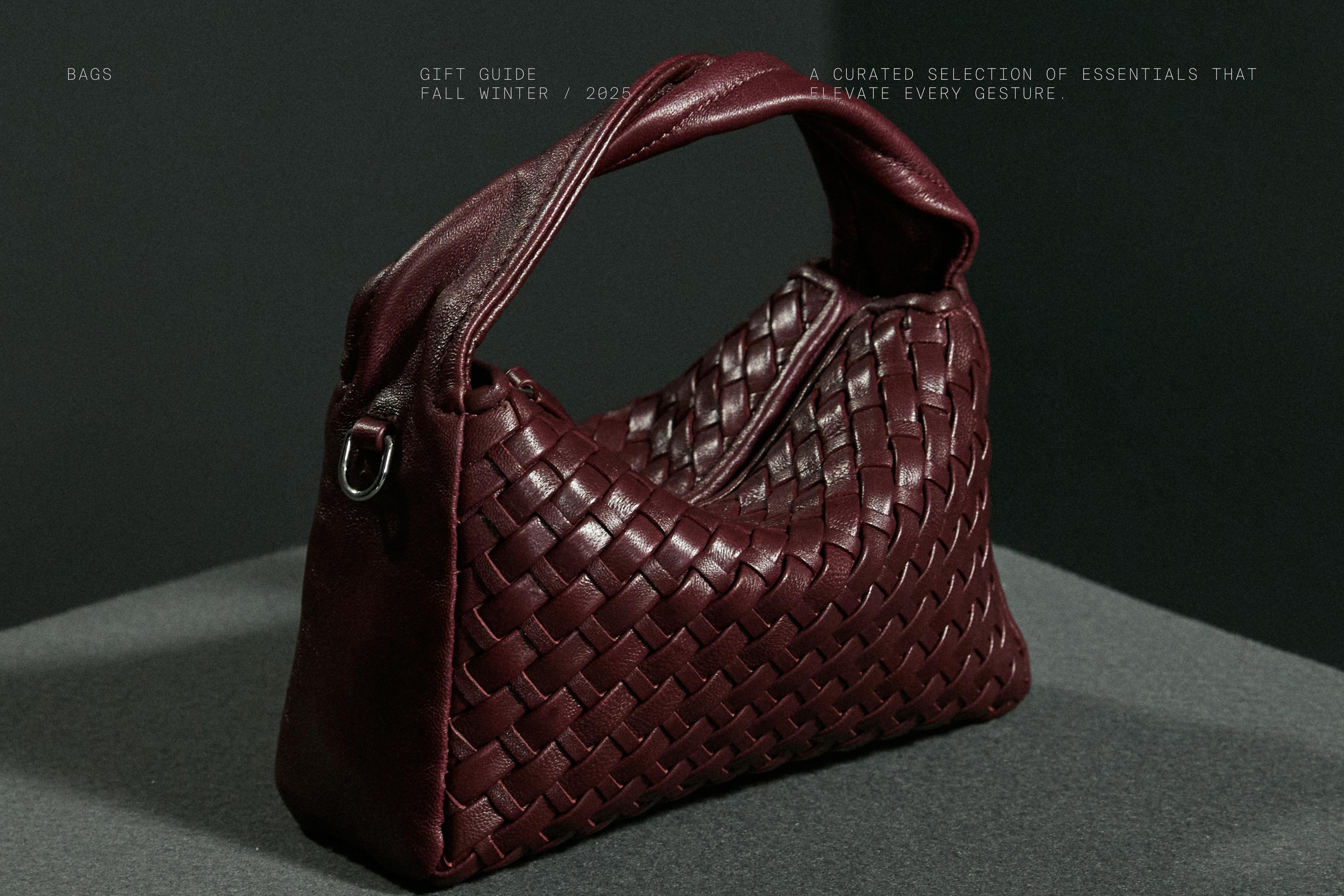 Bolso burdeos con diseño trenzado, asa superior y detalle de anilla metálica lateral. Texto visible: "GIFT GUIDE FALL WINTER / 2023".