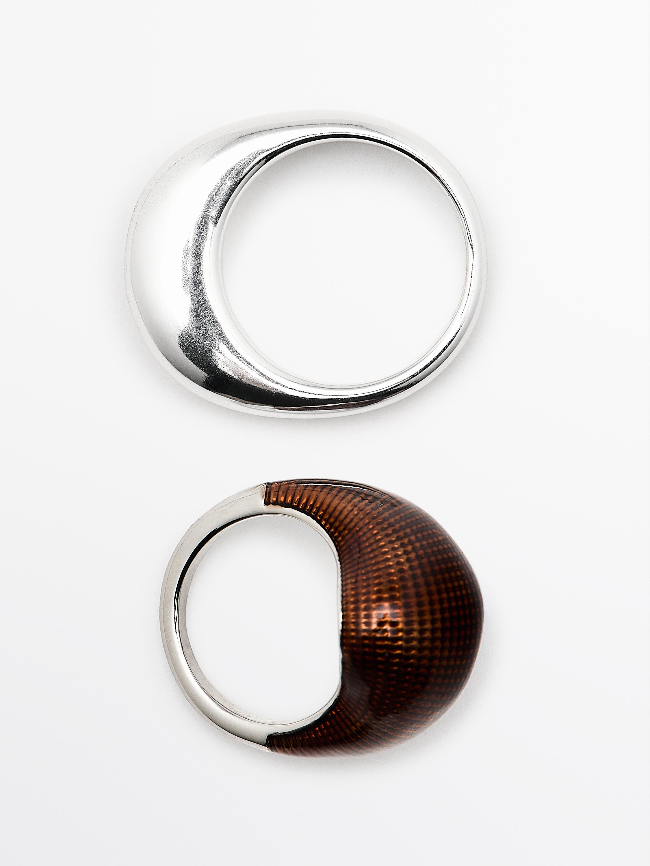 Δύο δαχτυλίδια, το ένα ασημένιο με λείο σχέδιο και το άλλο με καφέ ανάγλυφη κορυφή.